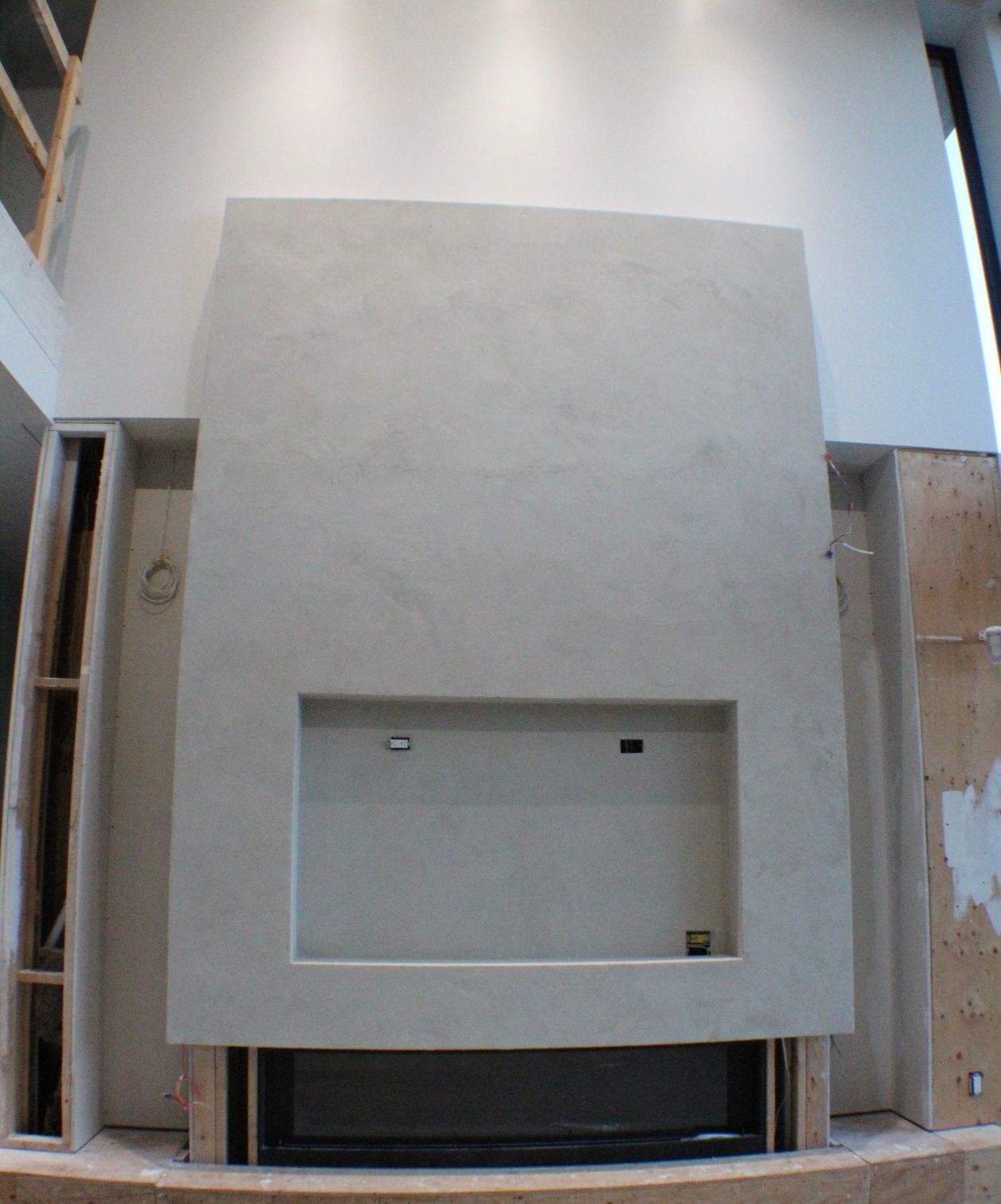 Cheminée gris clair avec un espace rectangulaire encastré, adossée à un mur blanc, en construction.