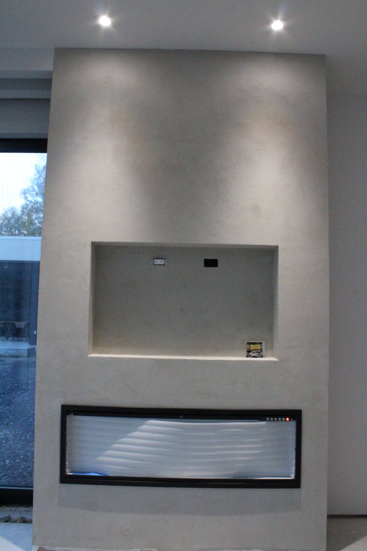 Une cheminée moderne encastrée dans un mur gris clair avec un coin TV encastré et des garnitures noires.