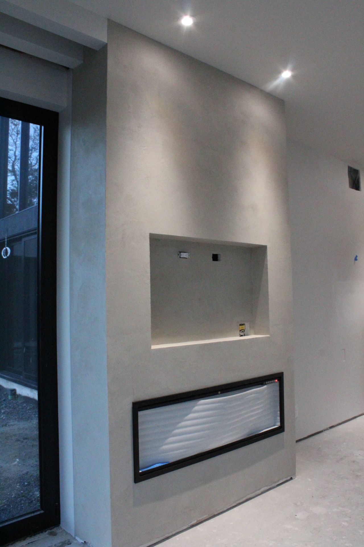 Intérieur moderne avec cheminée encastrée et niche TV dans un mur gris texturé.