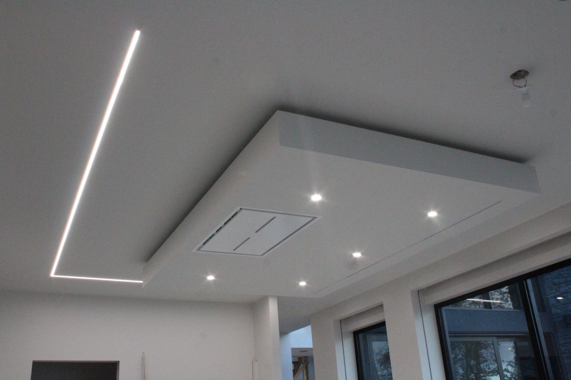 Plafond blanc moderne avec éclairage encastré, panneau rectangulaire et luminaire linéaire.
