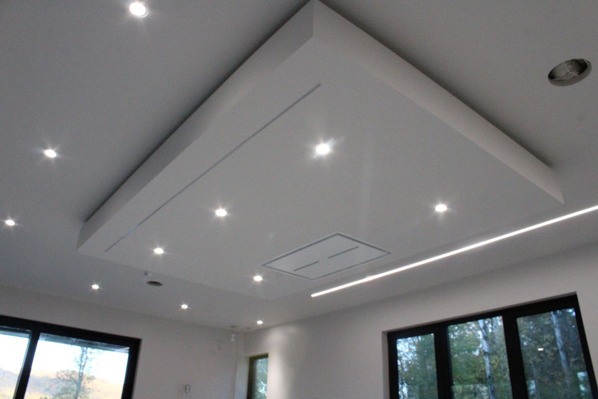 Plafond blanc avec éclairage encastré, un grand panneau et une hotte de cuisinière au-dessus d'une cuisine.