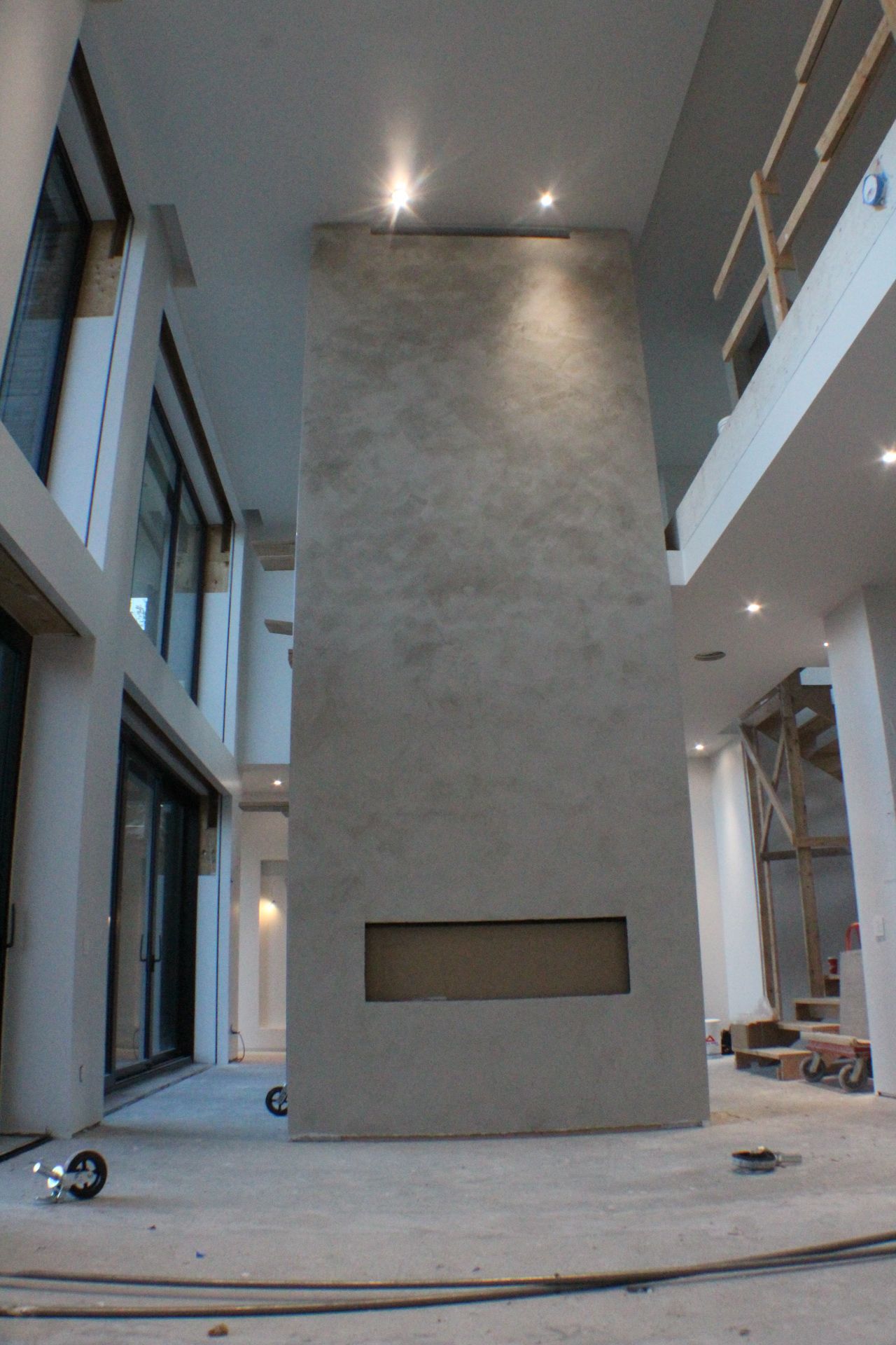 Cheminée haute, texturée et de couleur claire dans une grande pièce moderne inachevée avec de hauts plafonds et de grandes fenêtres.