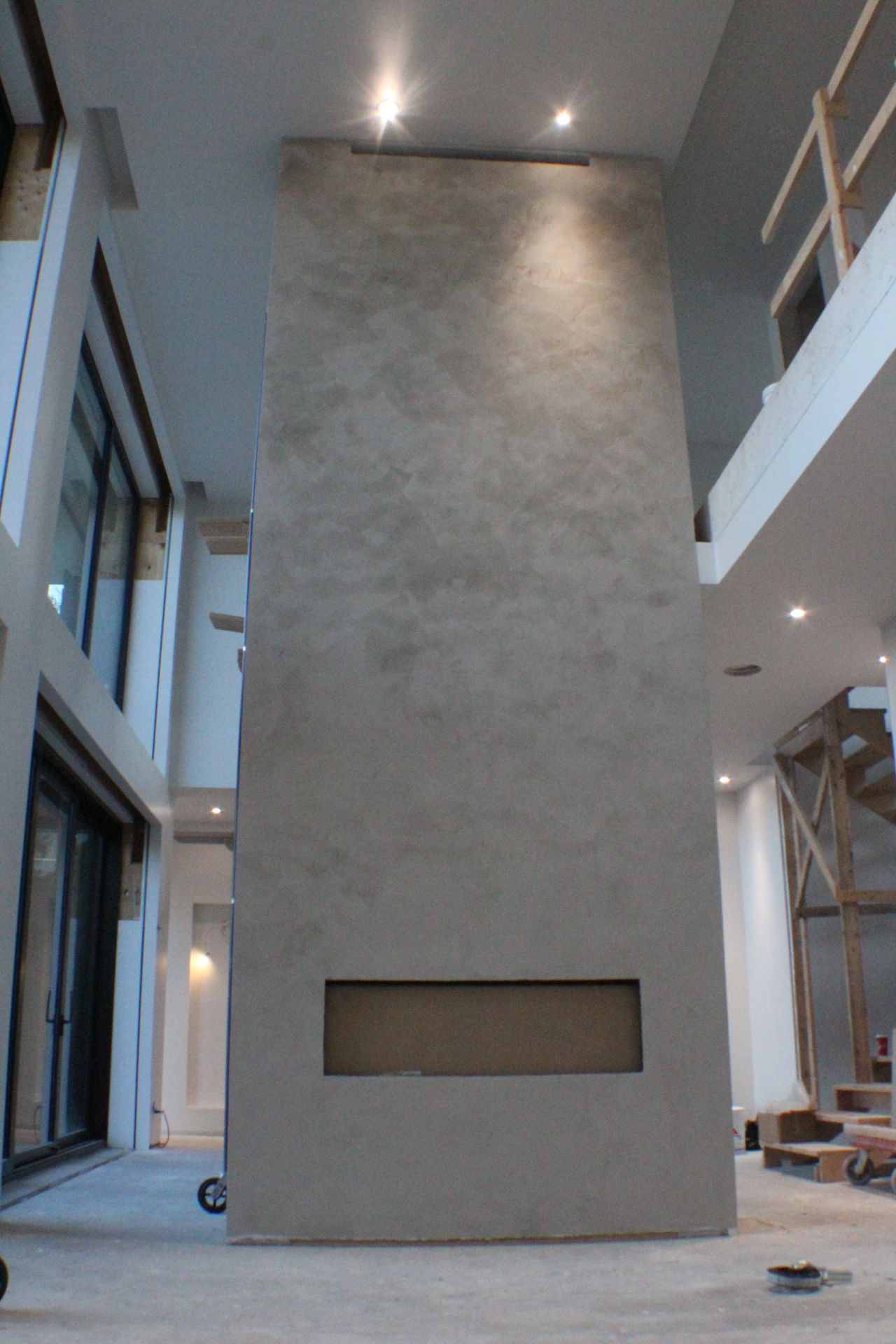 Grande cheminée grise à ouverture rectangulaire, dans une maison moderne à deux étages en construction.