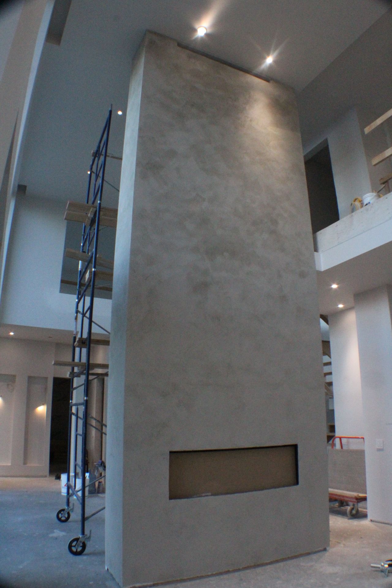 Grande cheminée en béton texturé avec une ouverture rectangulaire encastrée. Échafaudage à proximité.