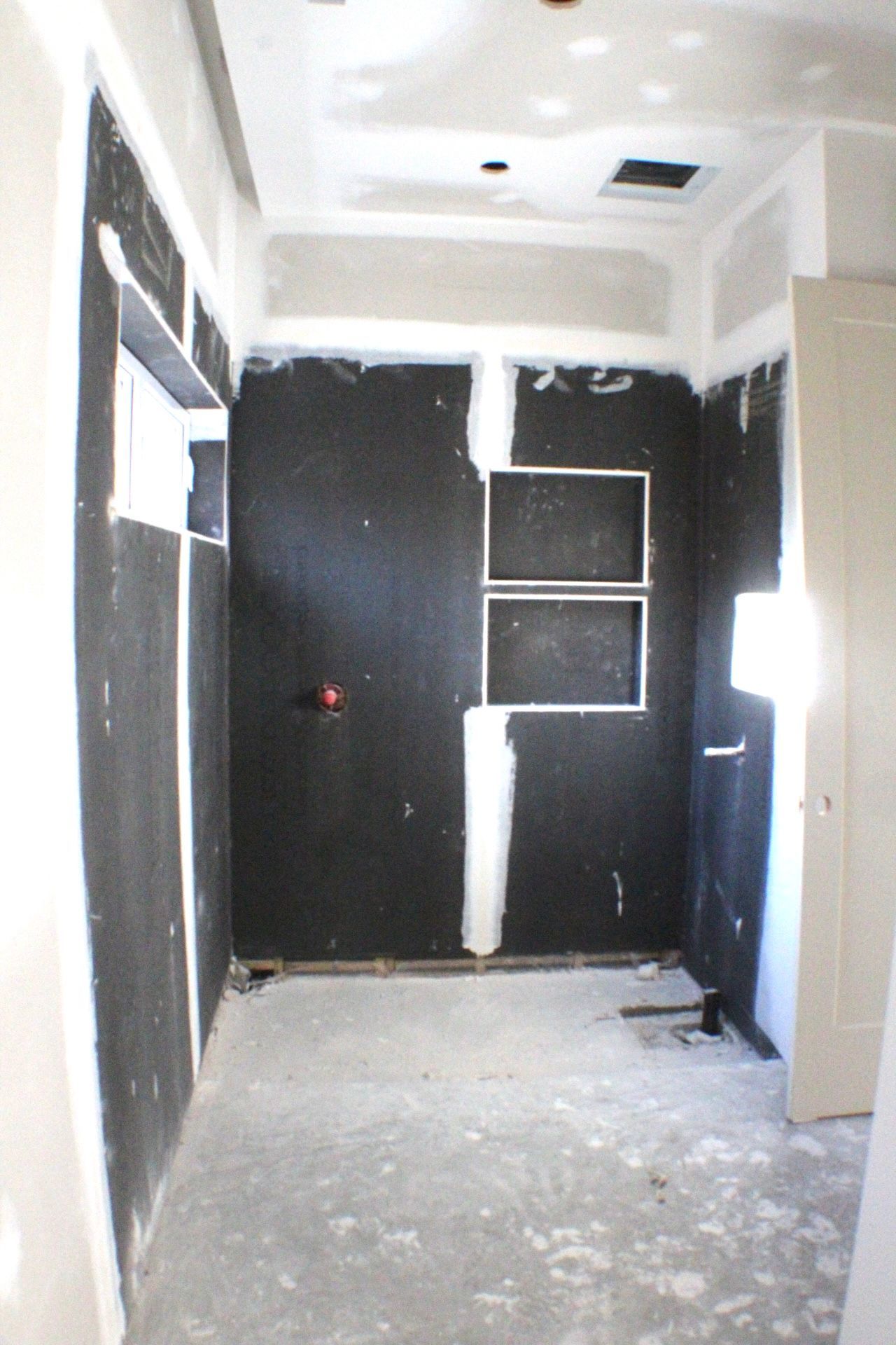 Salle de bain en construction, panneaux imperméables noirs, cloisons sèches, étagères encastrées, non fini.