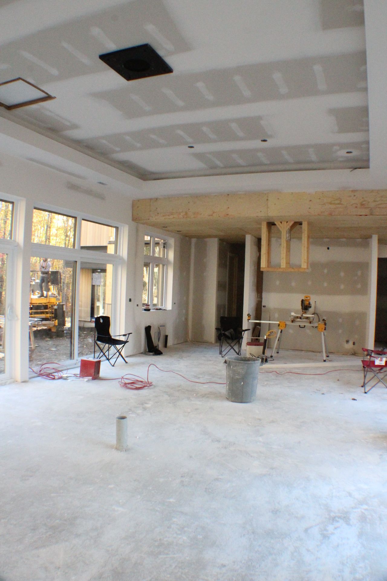 Chantier de construction intérieur avec murs, plafond et plancher non finis; fenêtres donnant sur une cour arrière.