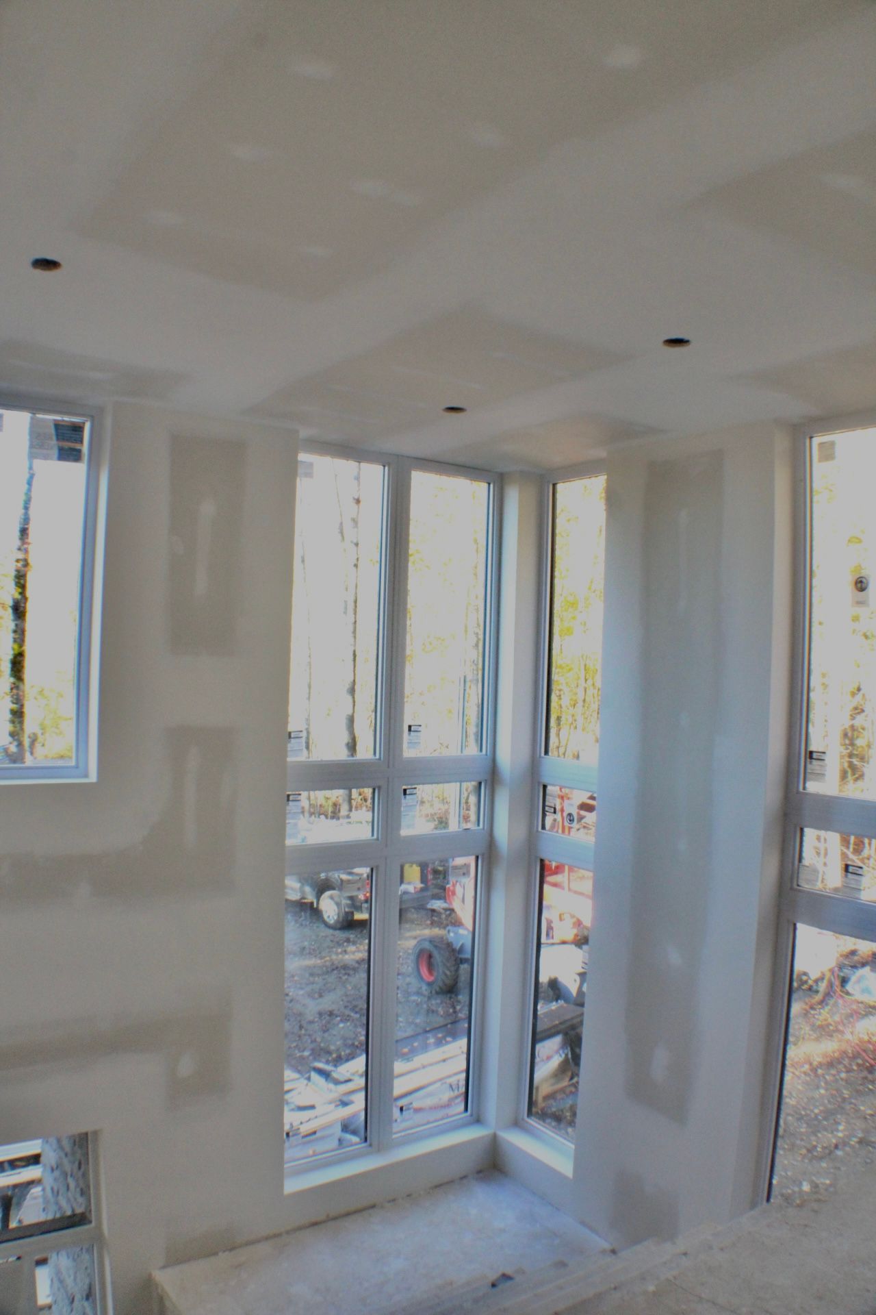 Intérieur d'un bâtiment en construction avec de grandes fenêtres et des murs en plaques de plâtre.