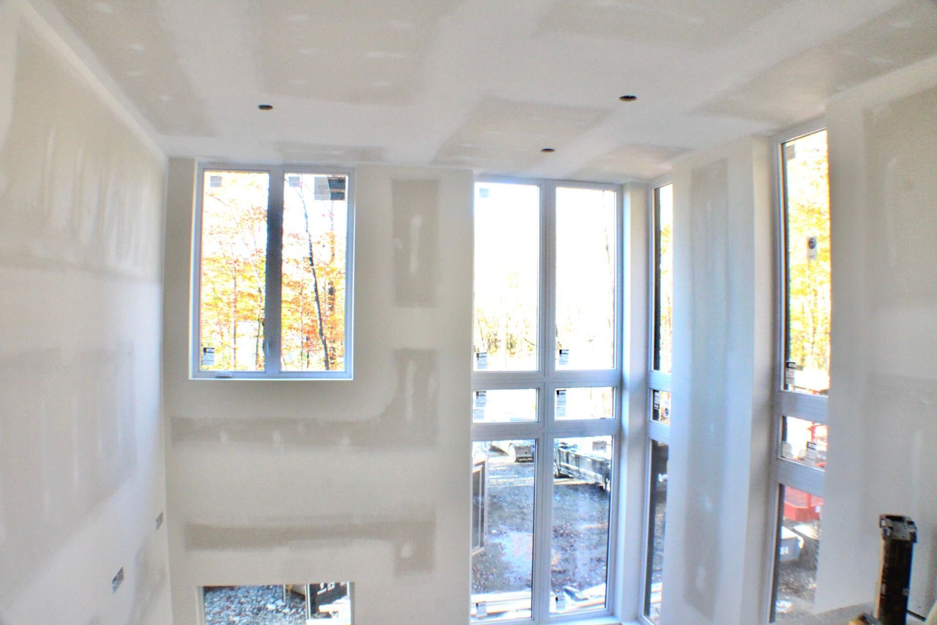 Vue intérieure d'une pièce avec cloisons sèches non finies, fenêtres et plafond encastré.