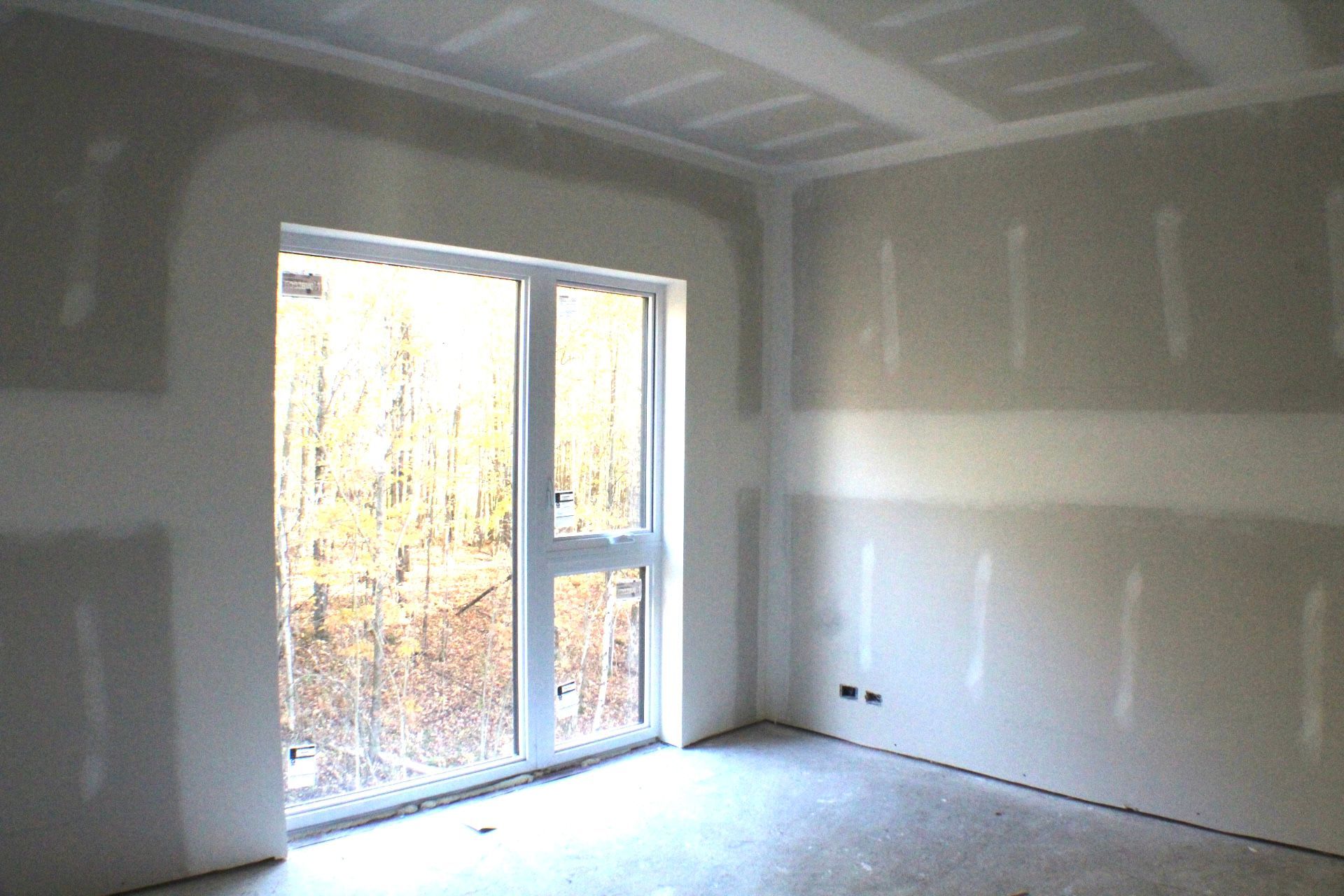 Pièce intérieure avec cloison sèche non finie, fenêtre et vue sur la forêt.