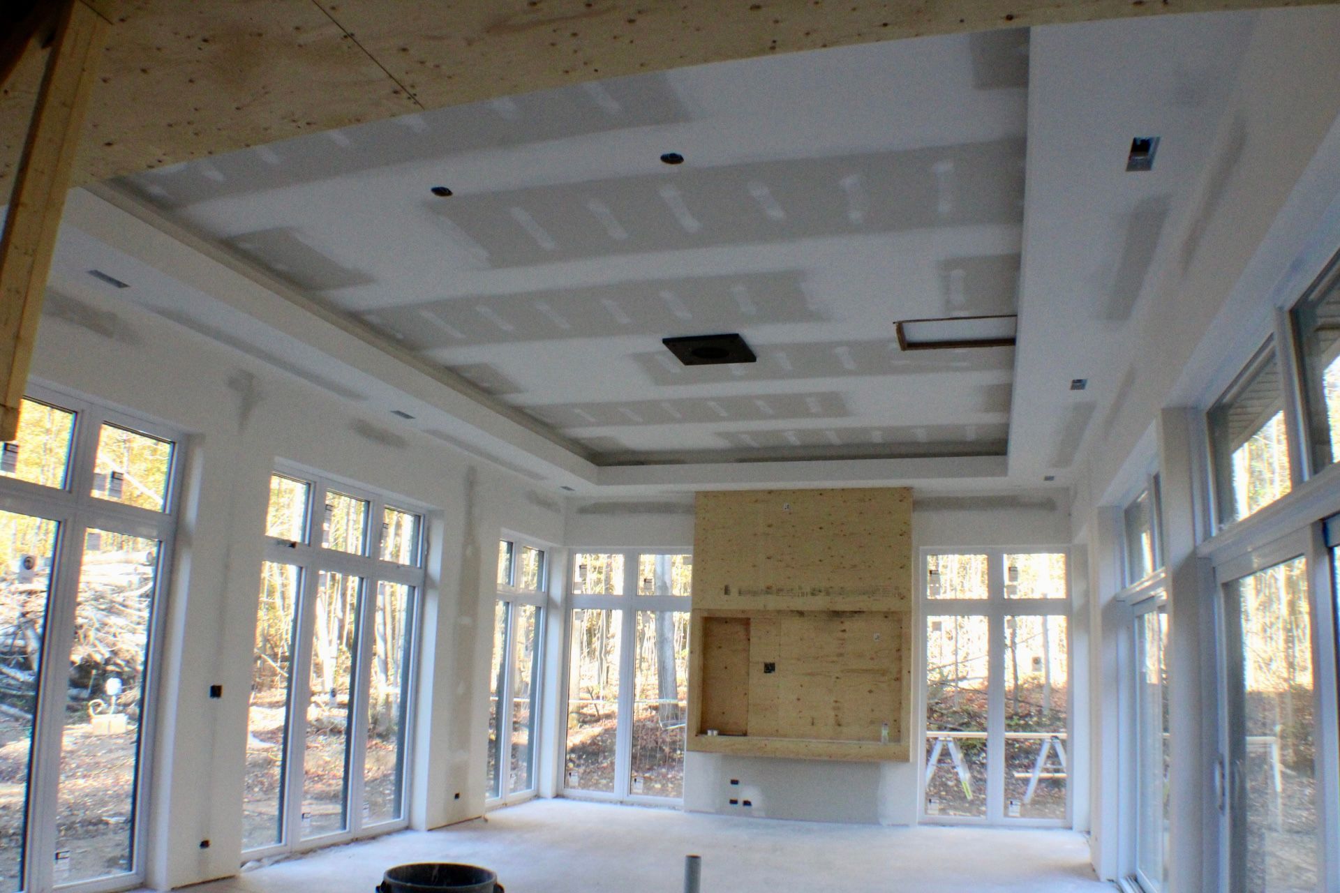 Chambre en construction avec plafond en plaques de plâtre, grandes fenêtres et foyer.