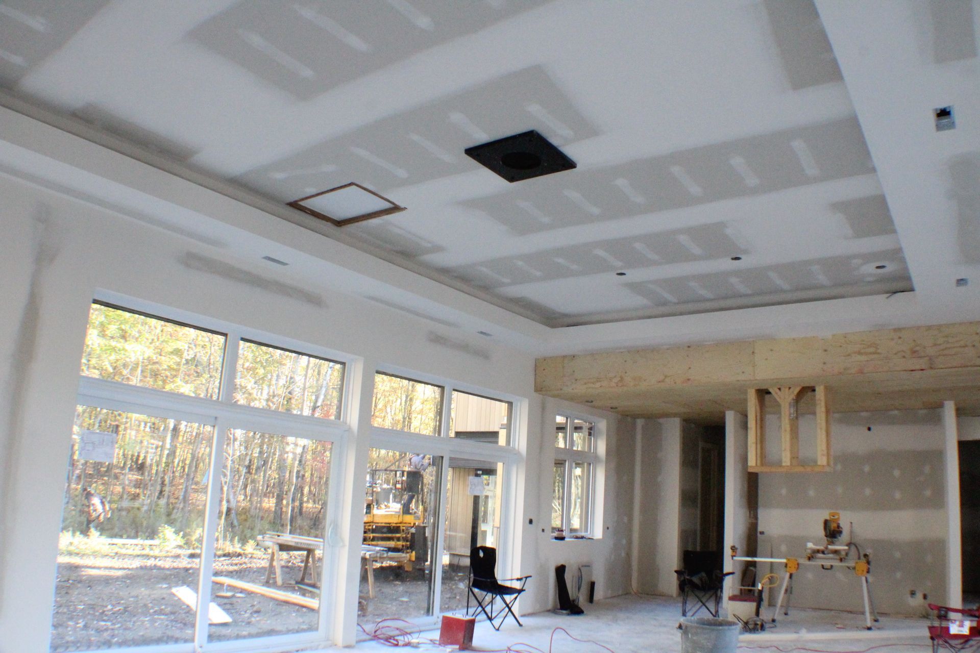 Chantier de construction intérieur avec plafond en plaques de plâtre, grandes fenêtres et outils.