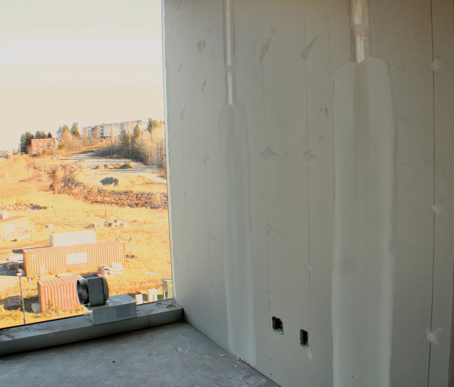 Vue intérieure d'une pièce inachevée avec cloisons sèches, fenêtre et vue extérieure.