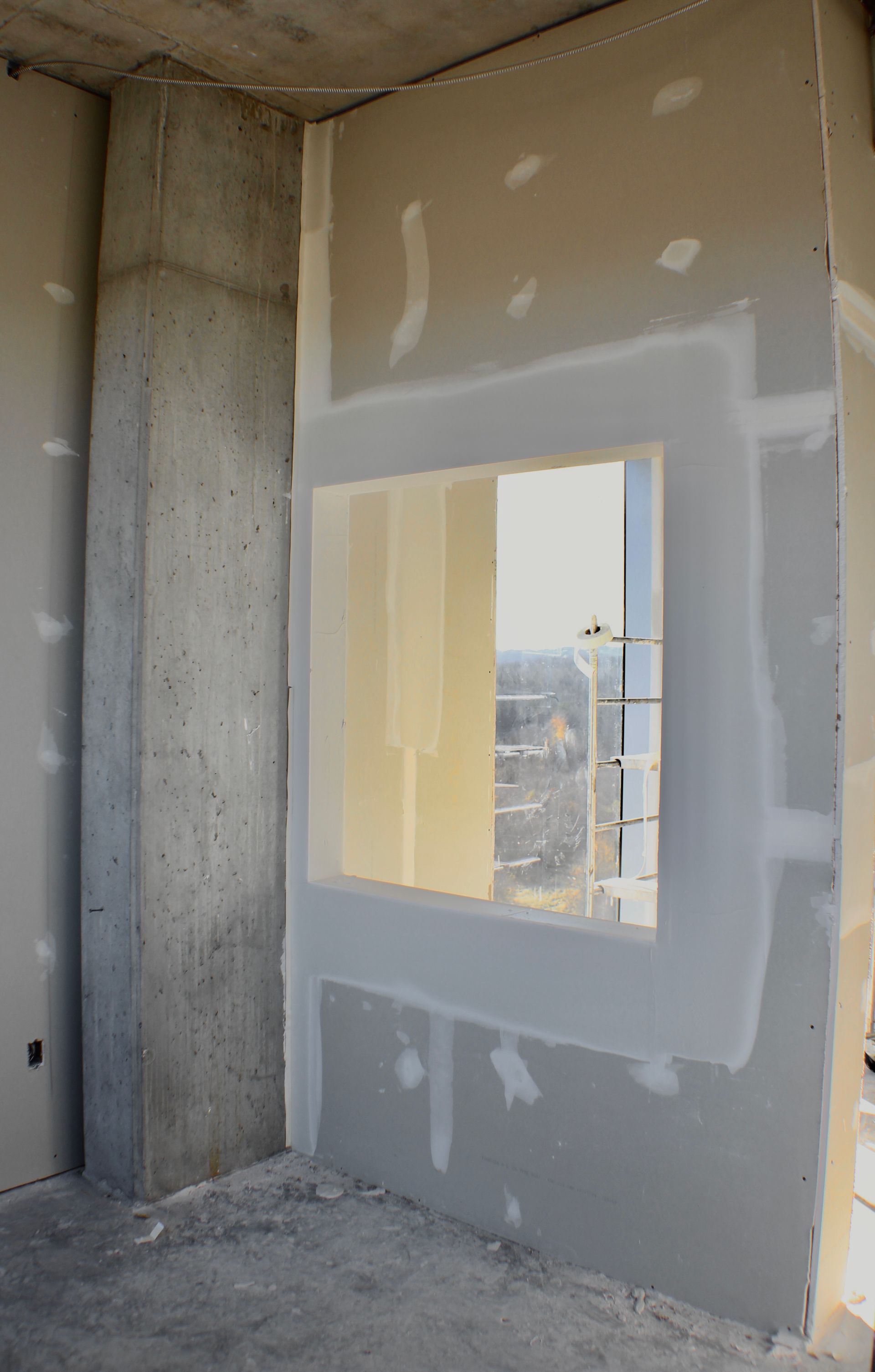 Vue intérieure d'un chantier de construction ; cloison sèche autour d'une fenêtre, poutre de support en béton.