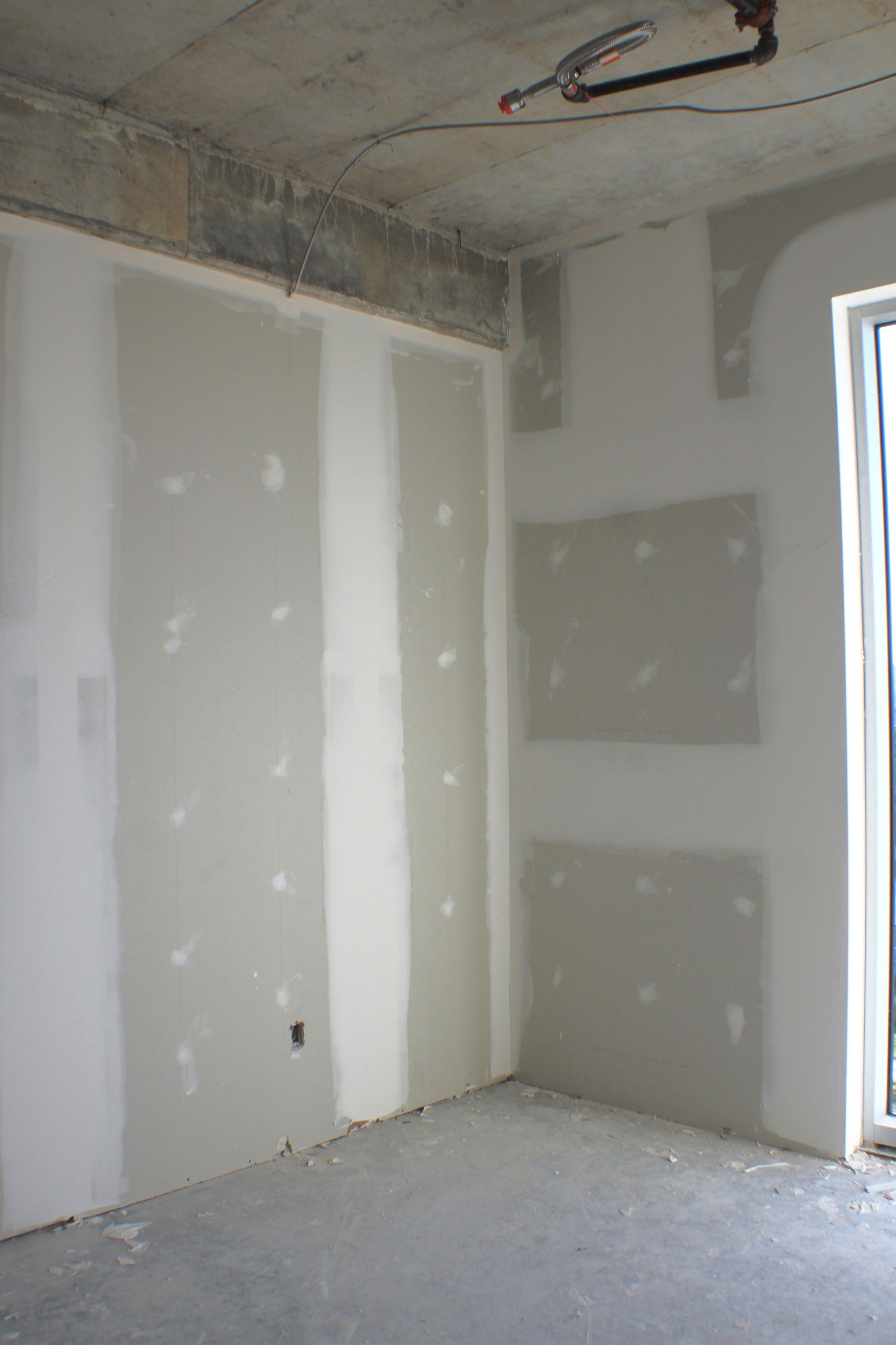 Intérieur d'une pièce en construction; cloisons sèches installées sur les murs; sol et plafond en béton.