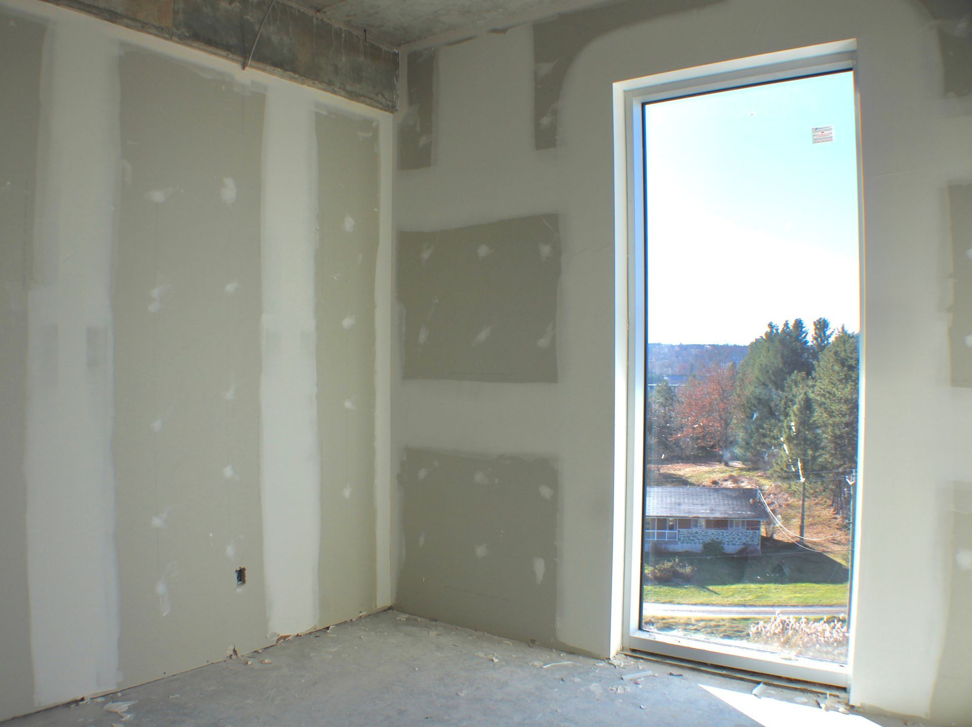 Aménagement intérieur d'une pièce avec cloisons sèches. Les encadrements de fenêtre offrent une vue sur des arbres et un bâtiment.