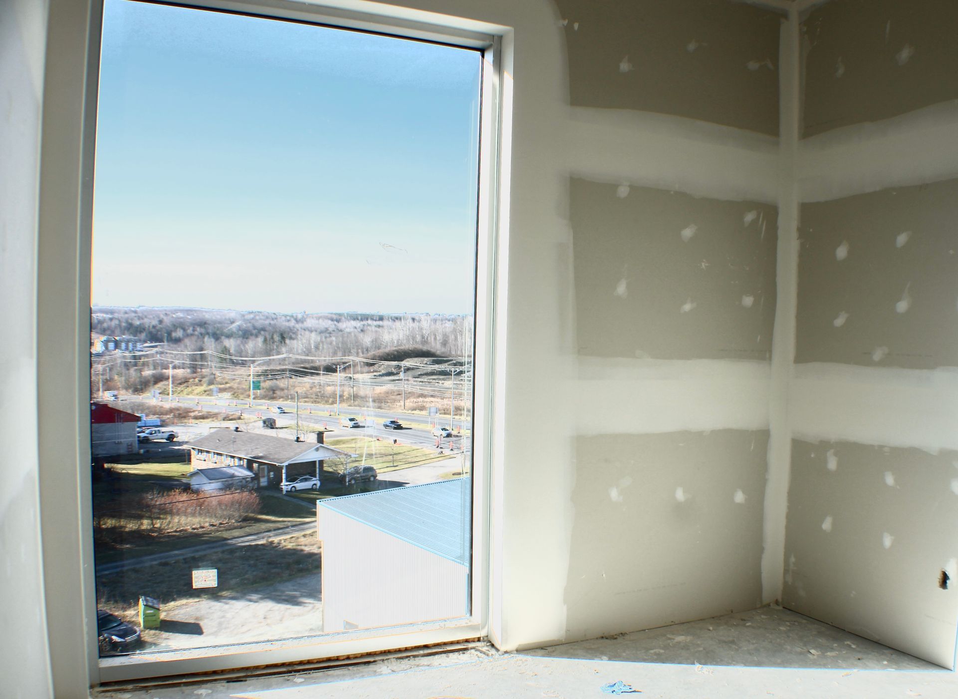 Vue intérieure : Pièce inachevée avec une grande fenêtre montrant un paysage urbain extérieur.