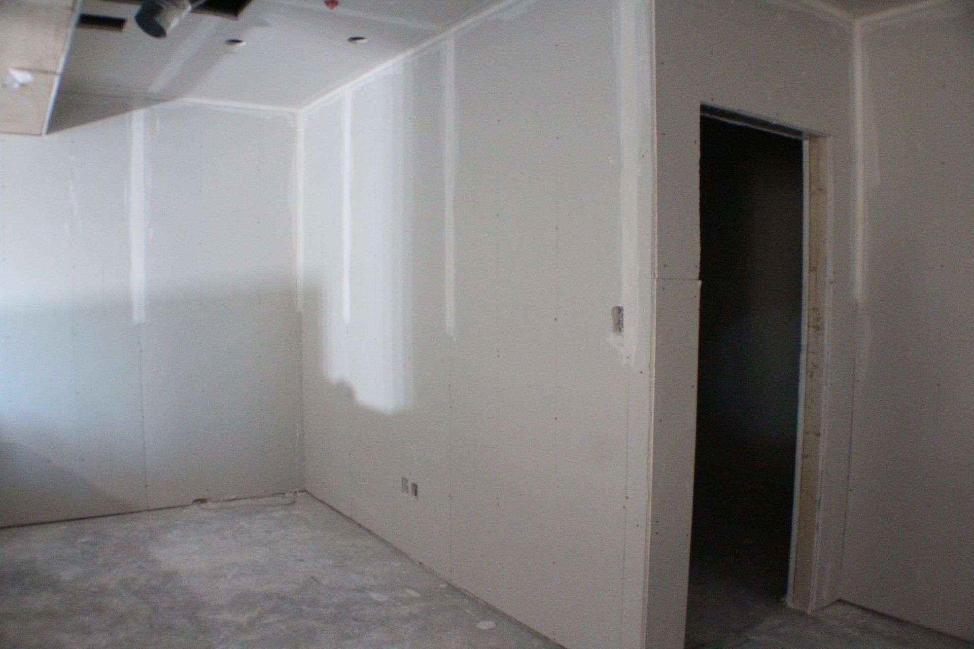 Vue intérieure d'une pièce en construction avec cloisons sèches et encadrement de porte. Sol en béton.