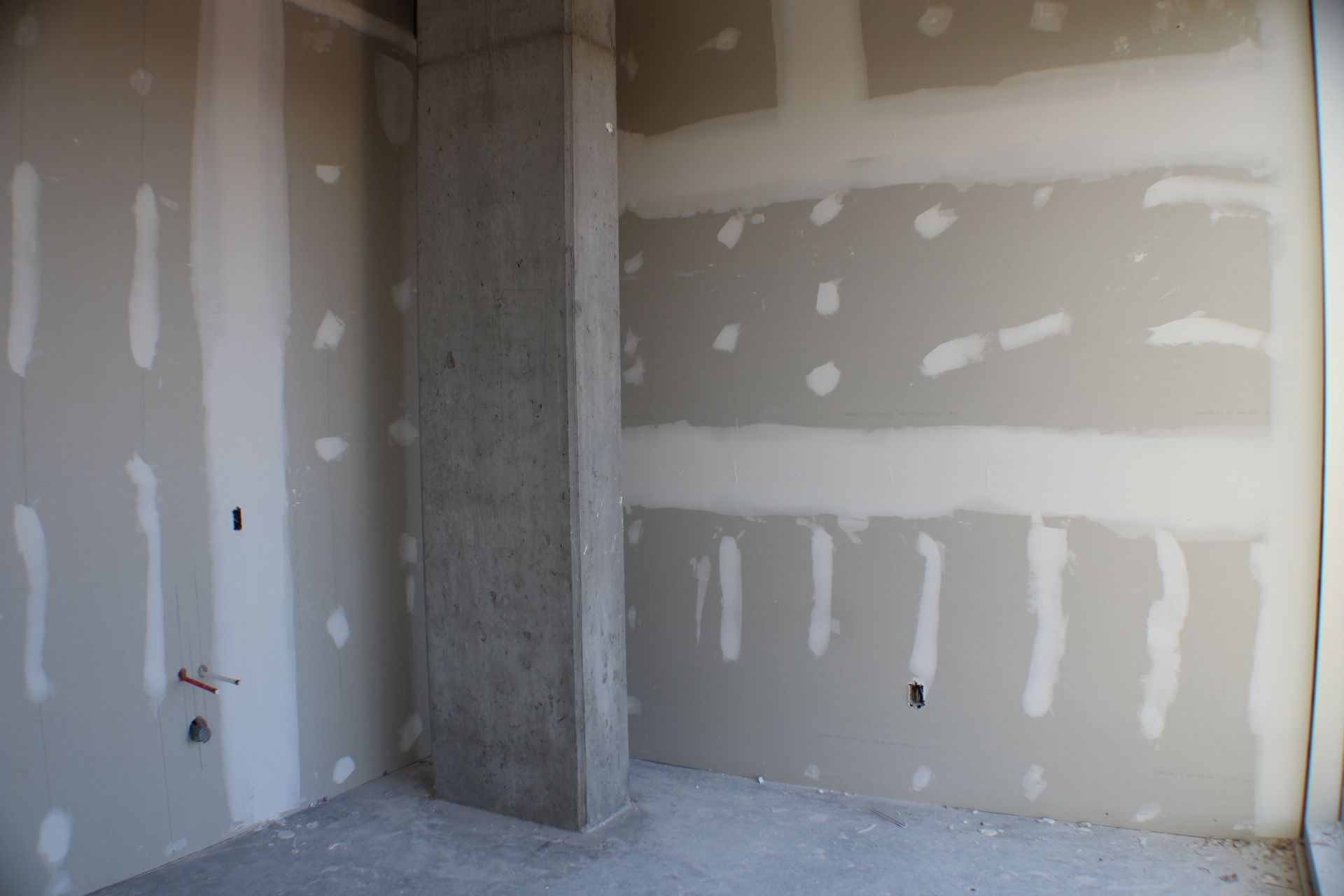 Construction intérieure avec cloisons sèches grises, composé à joints blanc et pilier en béton.