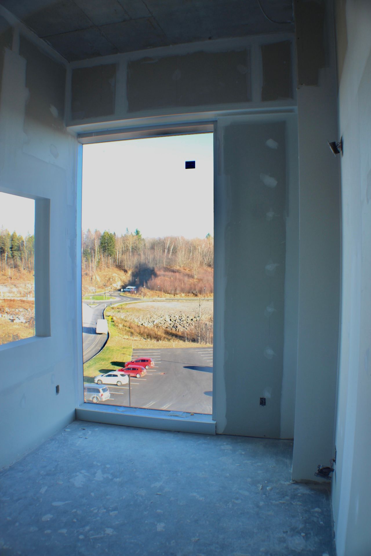 Vue intérieure d'une pièce en construction, grande fenêtre encadrant un paysage extérieur.