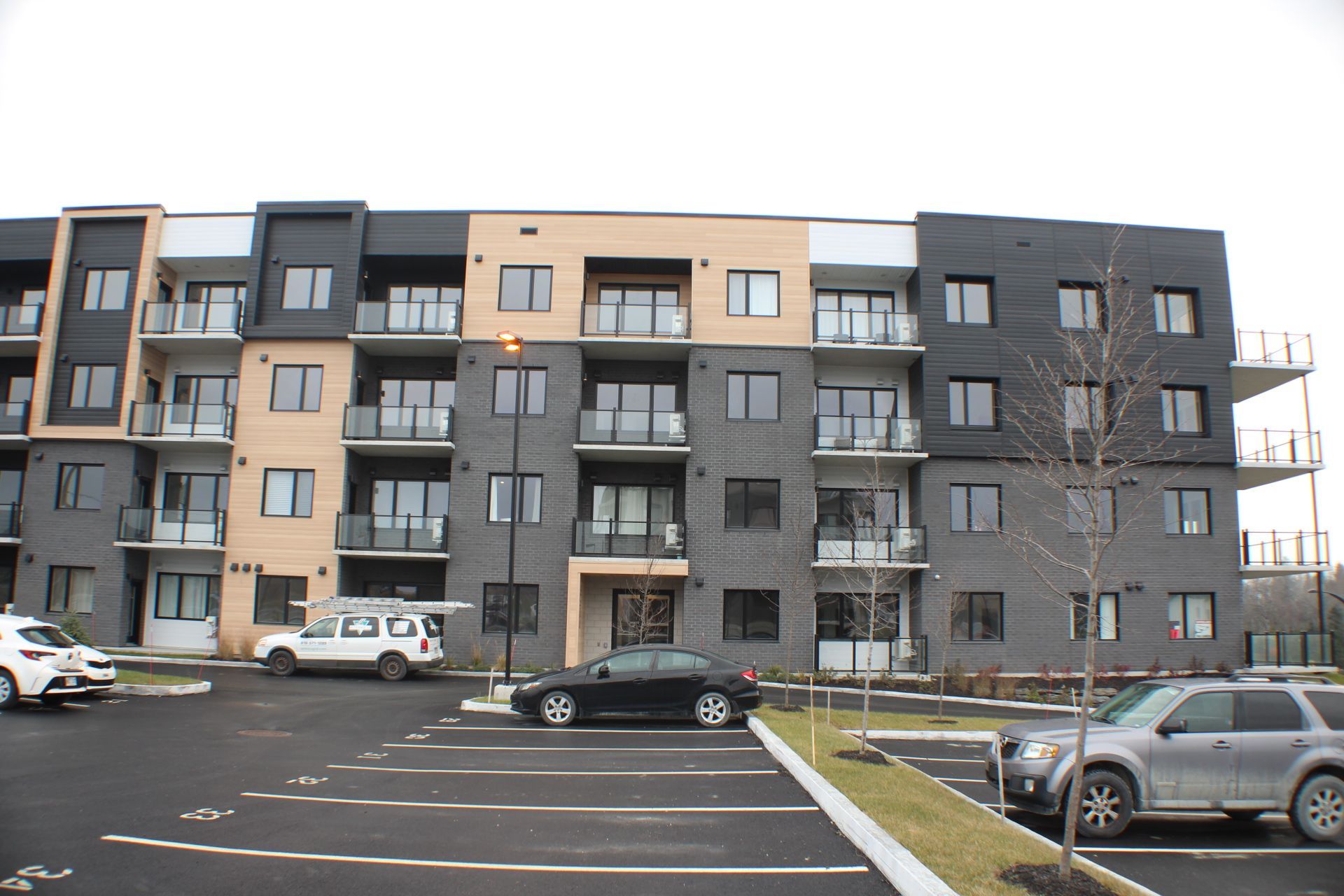 Immeuble d'habitation à la façade noire, grise et beige. Voitures garées sur un parking devant l'immeuble.