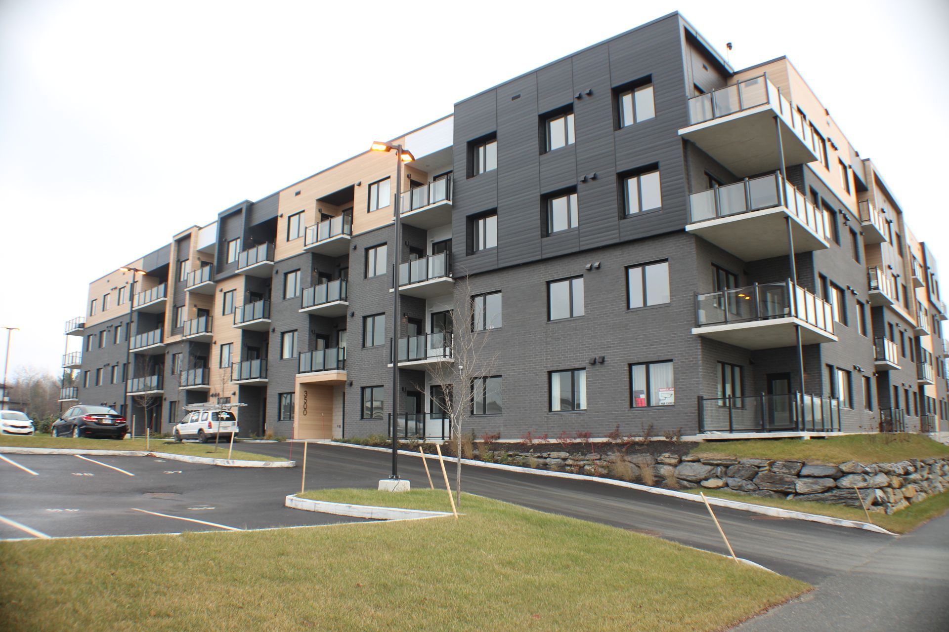 Immeuble d'appartements moderne avec façade noire et beige, balcons et parking.