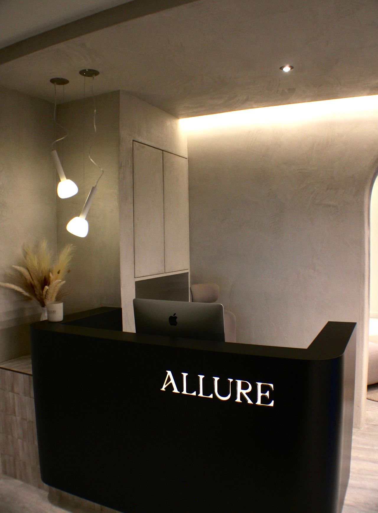 Comptoir de réception noir avec logo « ALLURE », armoires blanches et lumières suspendues.