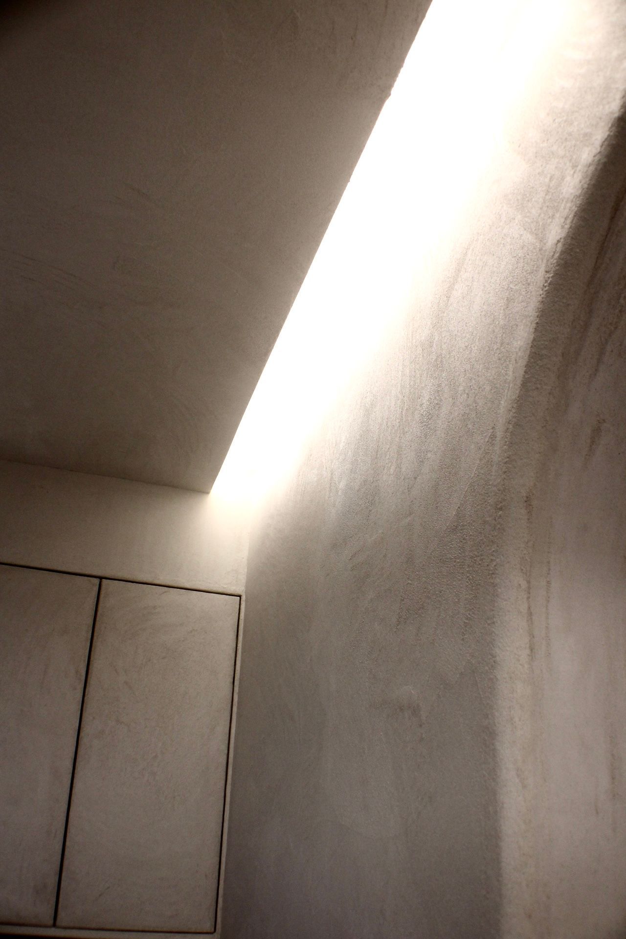 Un éclairage encastré au plafond illumine un mur blanc texturé et une armoire.