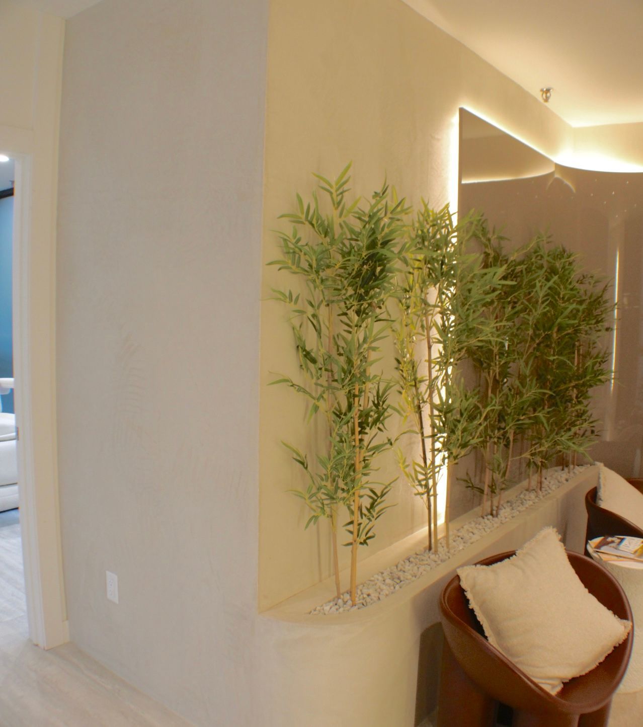 Intérieur avec des plantes de bambou en pot, des murs de couleur claire et un coin salon avec un oreiller blanc.