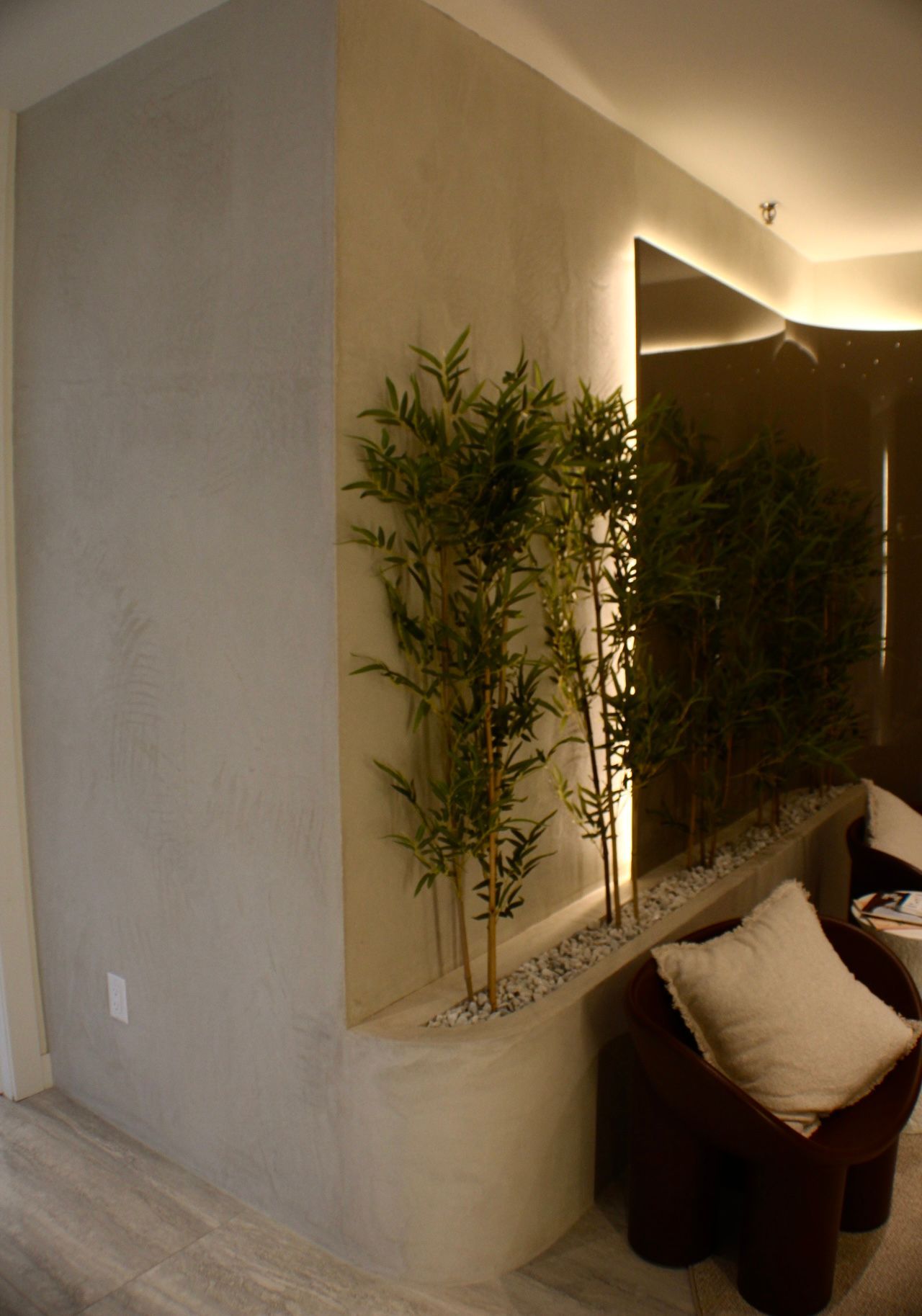 Salon d'angle avec des plantes en bambou, un mur en miroir et une chaise marron avec un coussin blanc.