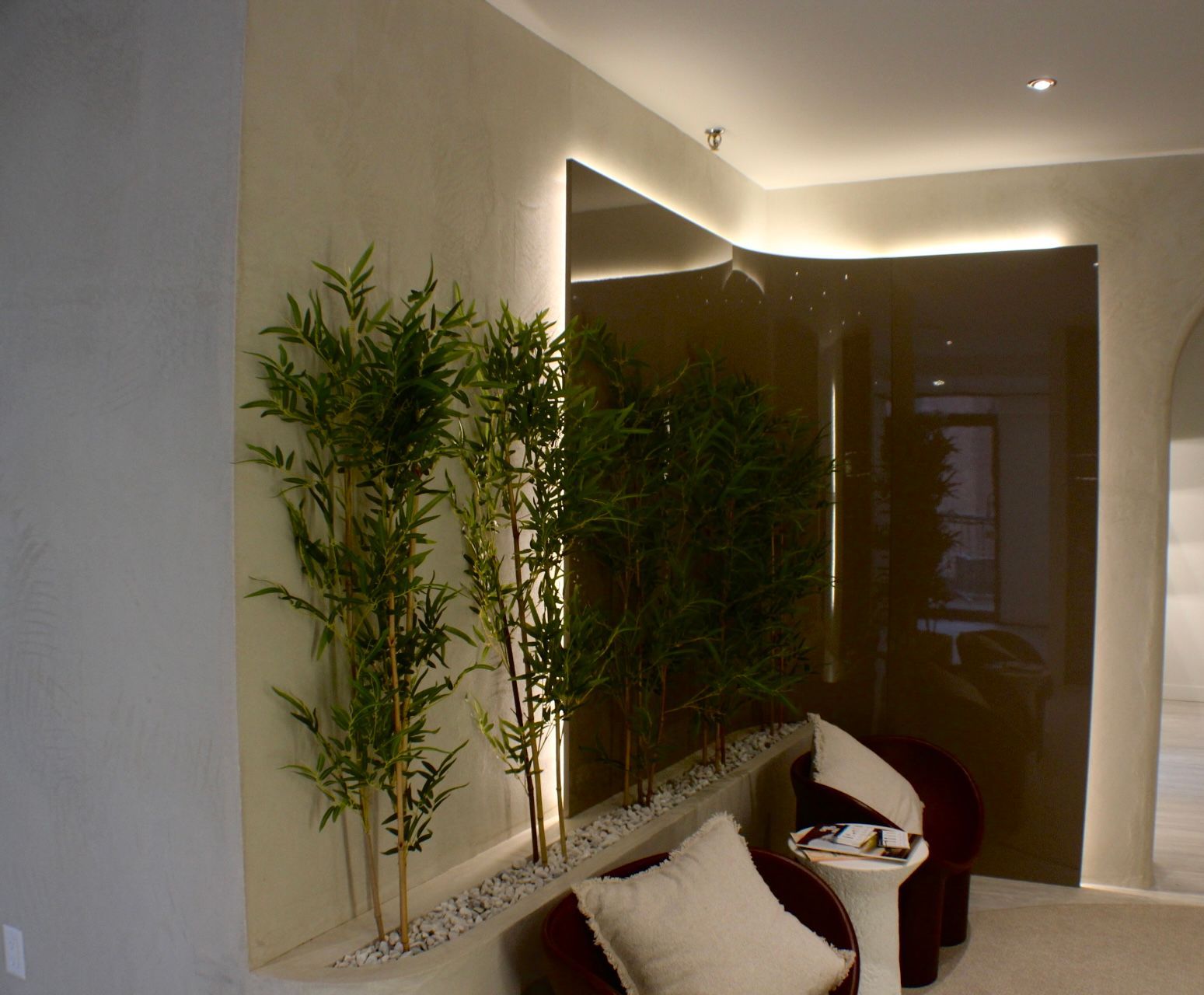Espace intérieur avec des plantes en bambou, un mur en miroir marron et des sièges avec des oreillers.