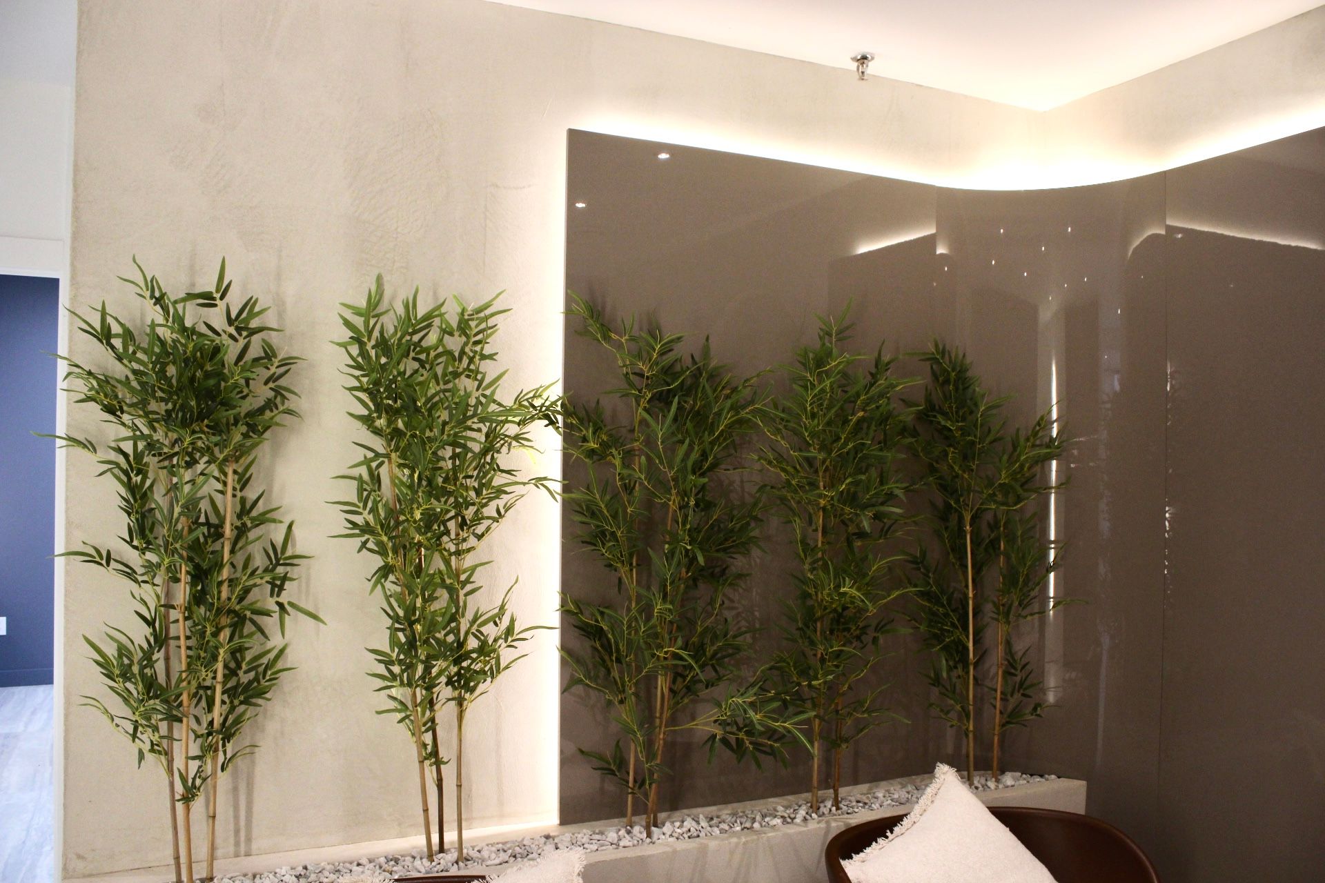 Plantes de bambou dans un décor intérieur moderne avec des murs gris, des pierres blanches et une chaise en cuir marron.