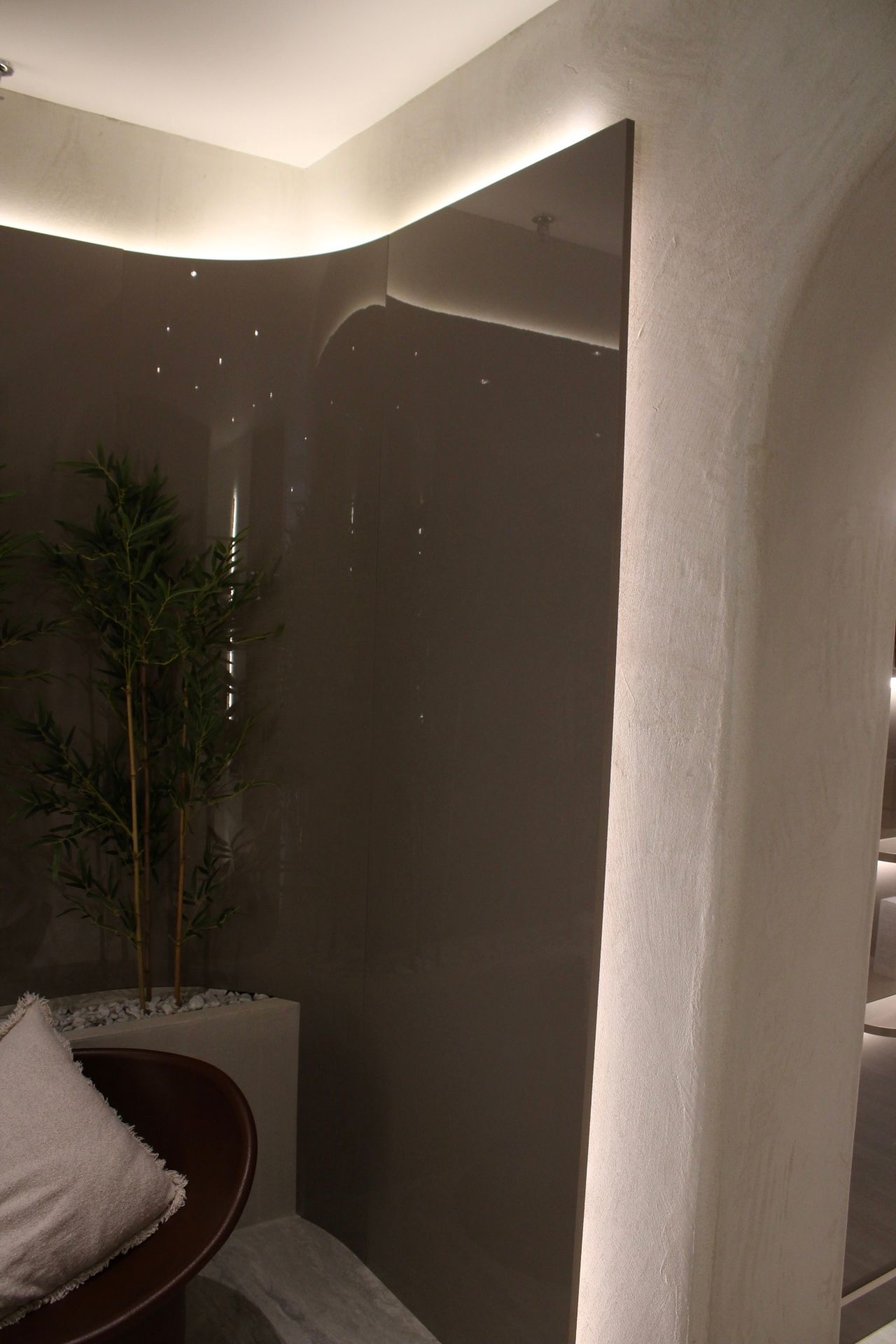 Intérieur moderne avec mur gris, arche et petite plante de bambou dans une jardinière blanche, éclairé par un éclairage doux.