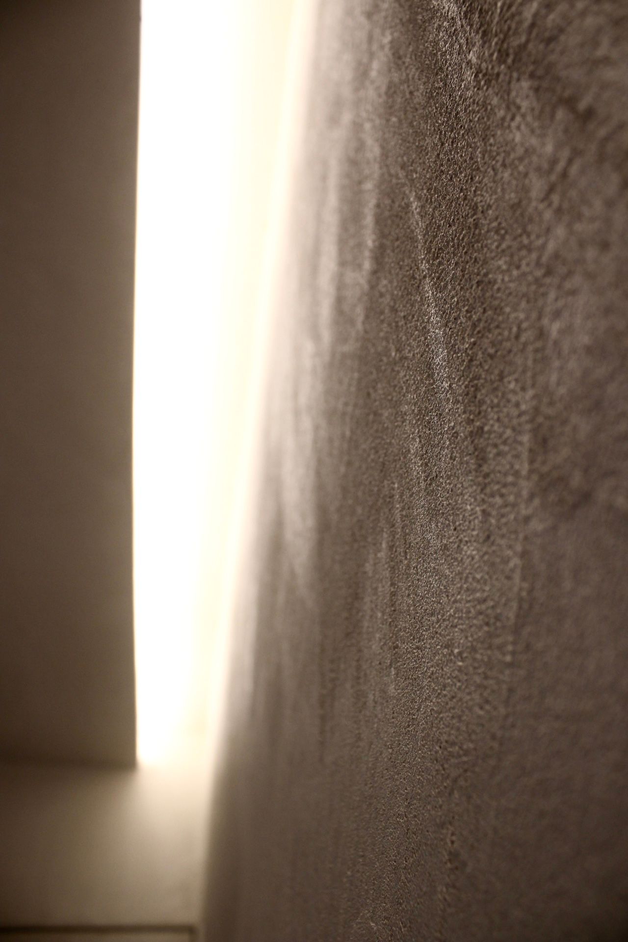 Gros plan d'un mur gris texturé avec une lumière vive provenant de la gauche.