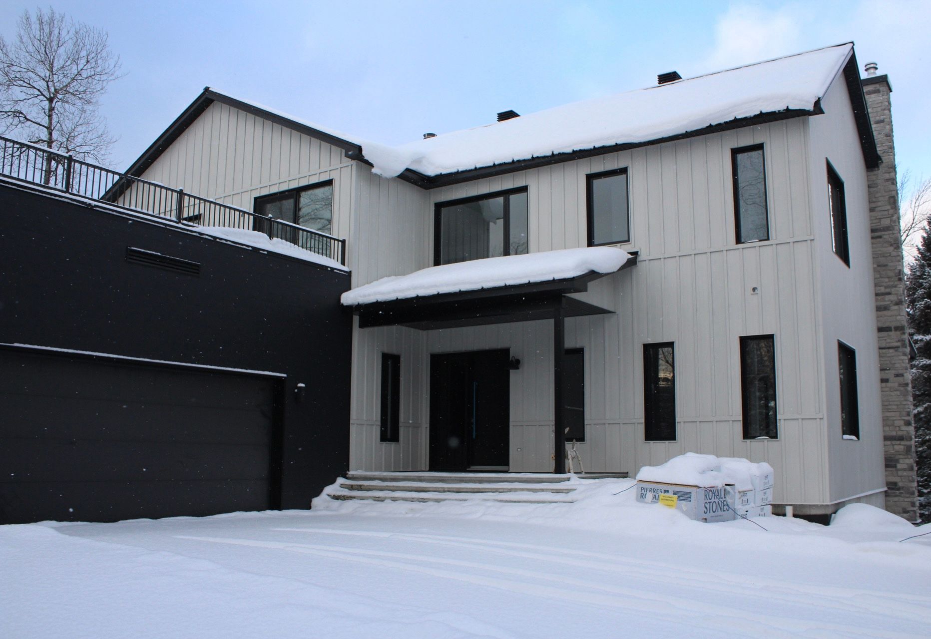 Maison blanche aux touches noires, toit enneigé et porte de garage. Décor hivernal.