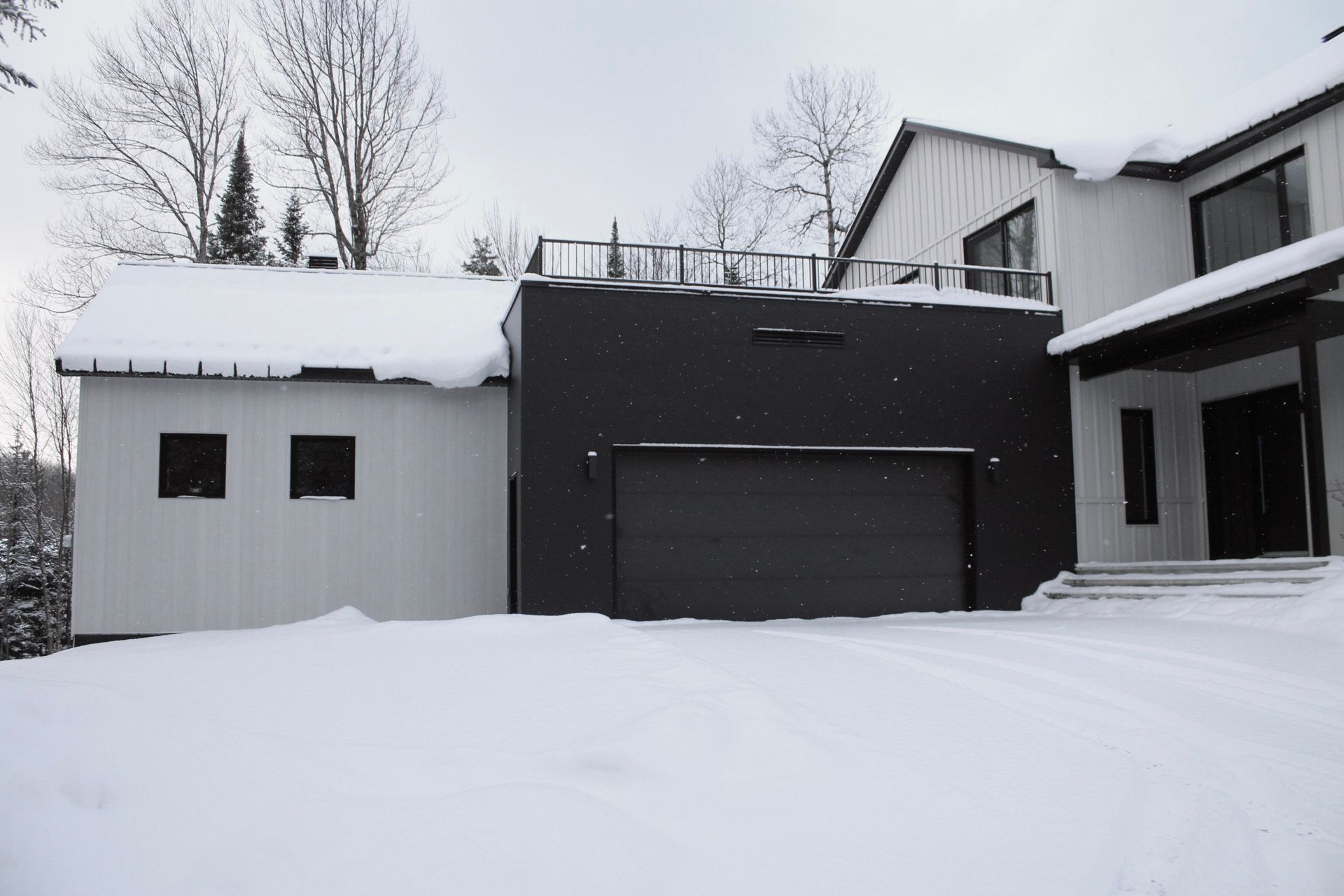 Maison moderne recouverte de neige avec extérieur blanc et noir, garage et terrasse sur le toit.