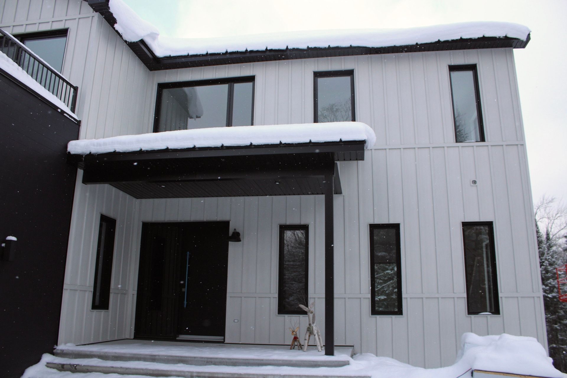 Maison blanche avec des garnitures et des fenêtres noires, recouverte de neige.