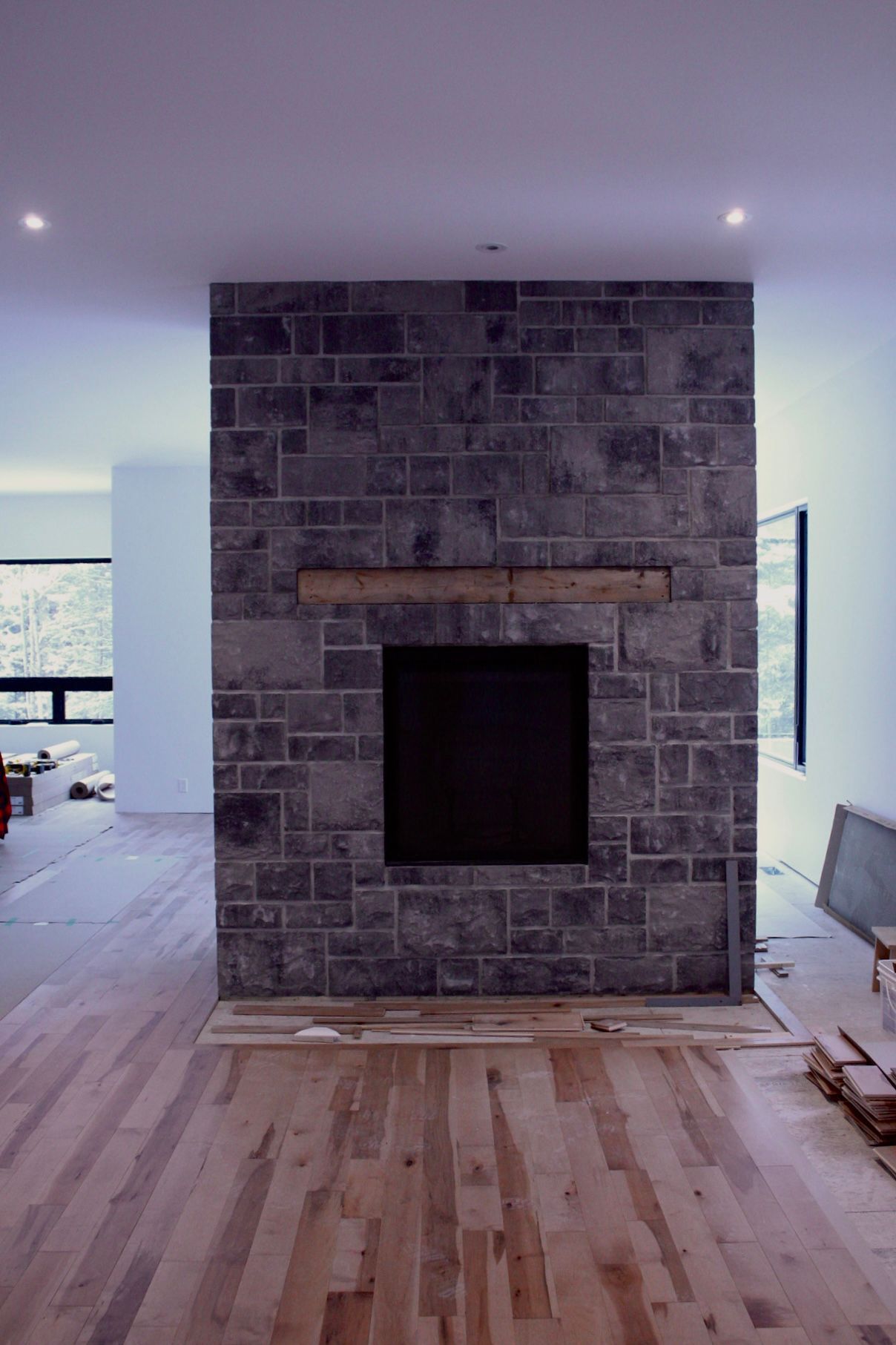 Cheminée en pierre avec manteau en bois et foyer noir, dans une pièce avec parquet.