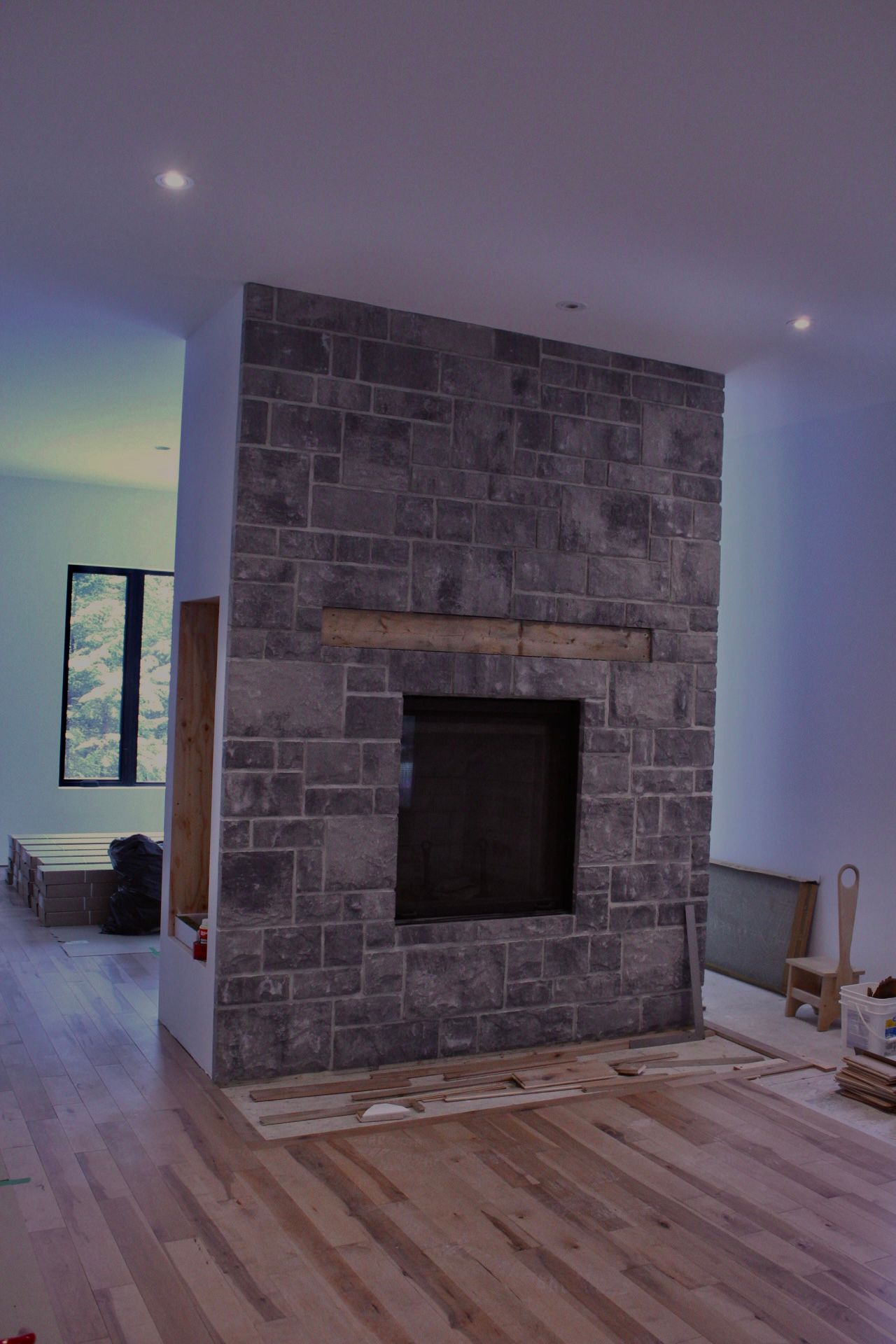 Cheminée en pierre avec brique gris foncé, plancher en bois et une fenêtre en arrière-plan.