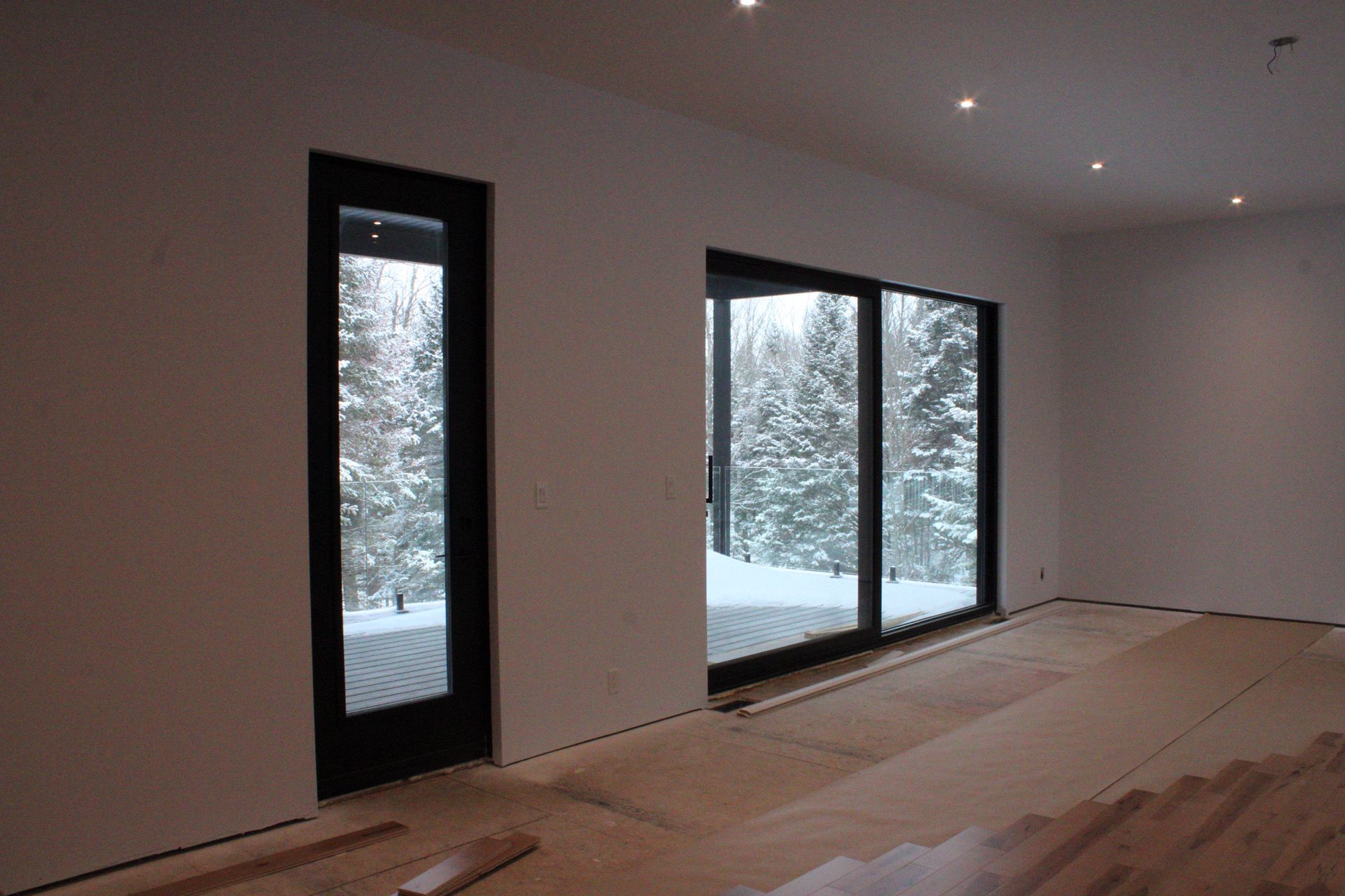 Vue intérieure d'une pièce avec de grandes fenêtres et une porte, donnant sur un paysage enneigé.