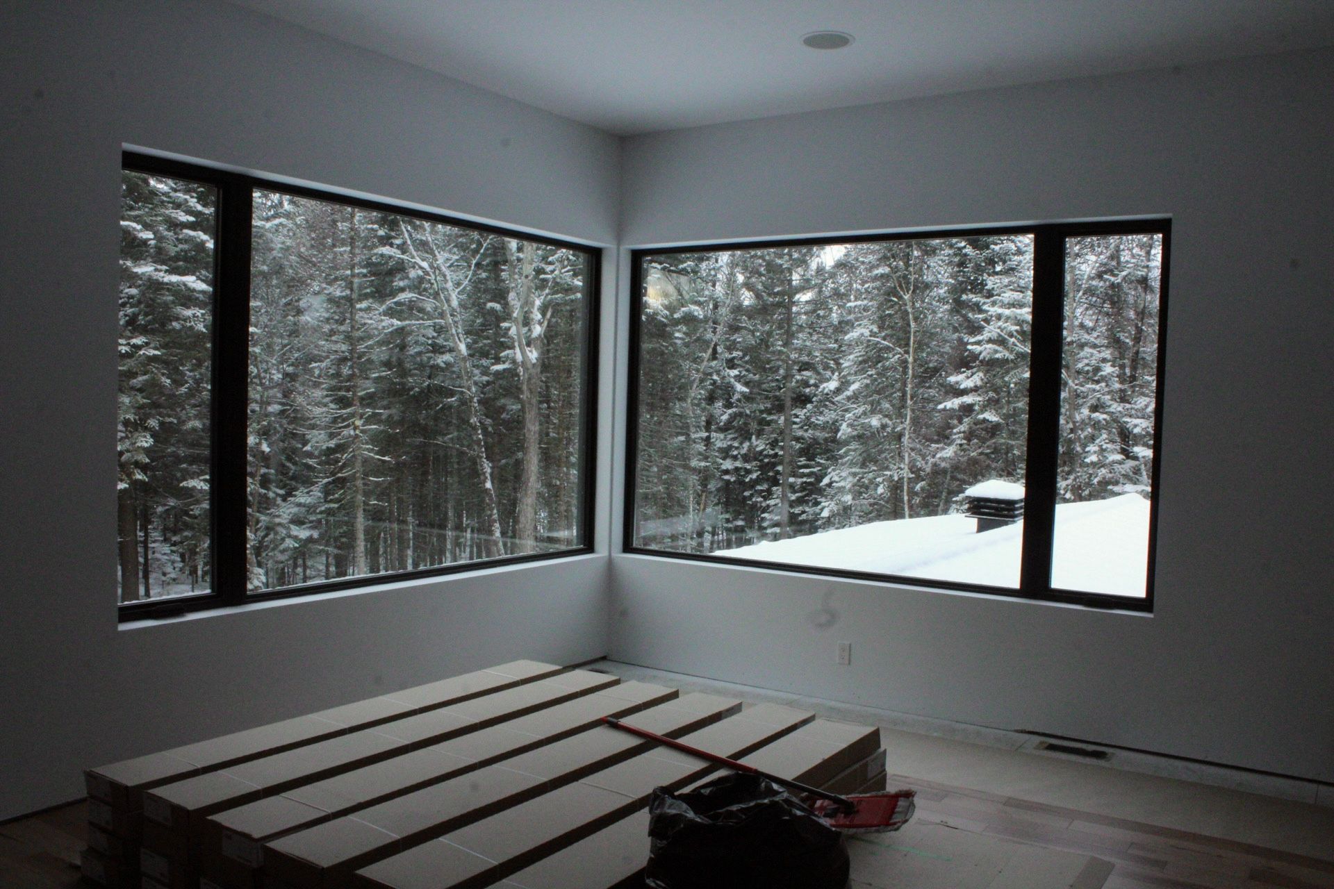 Chambre d'angle avec de grandes fenêtres donnant sur une forêt enneigée. Un lit plateforme est posé au sol.