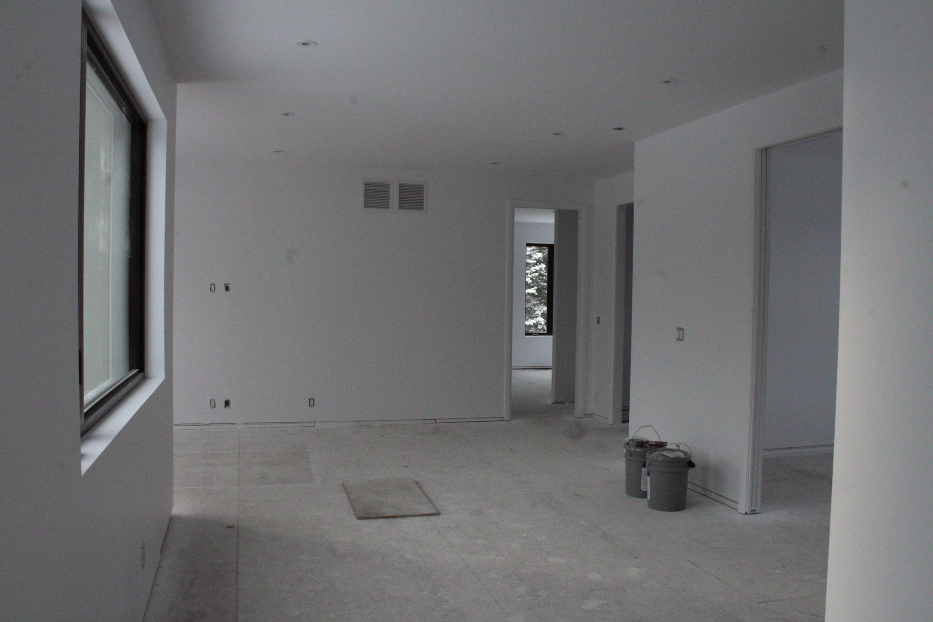 Pièce intérieure vide, murs blancs, sol en béton, construction inachevée, porte, fenêtre.