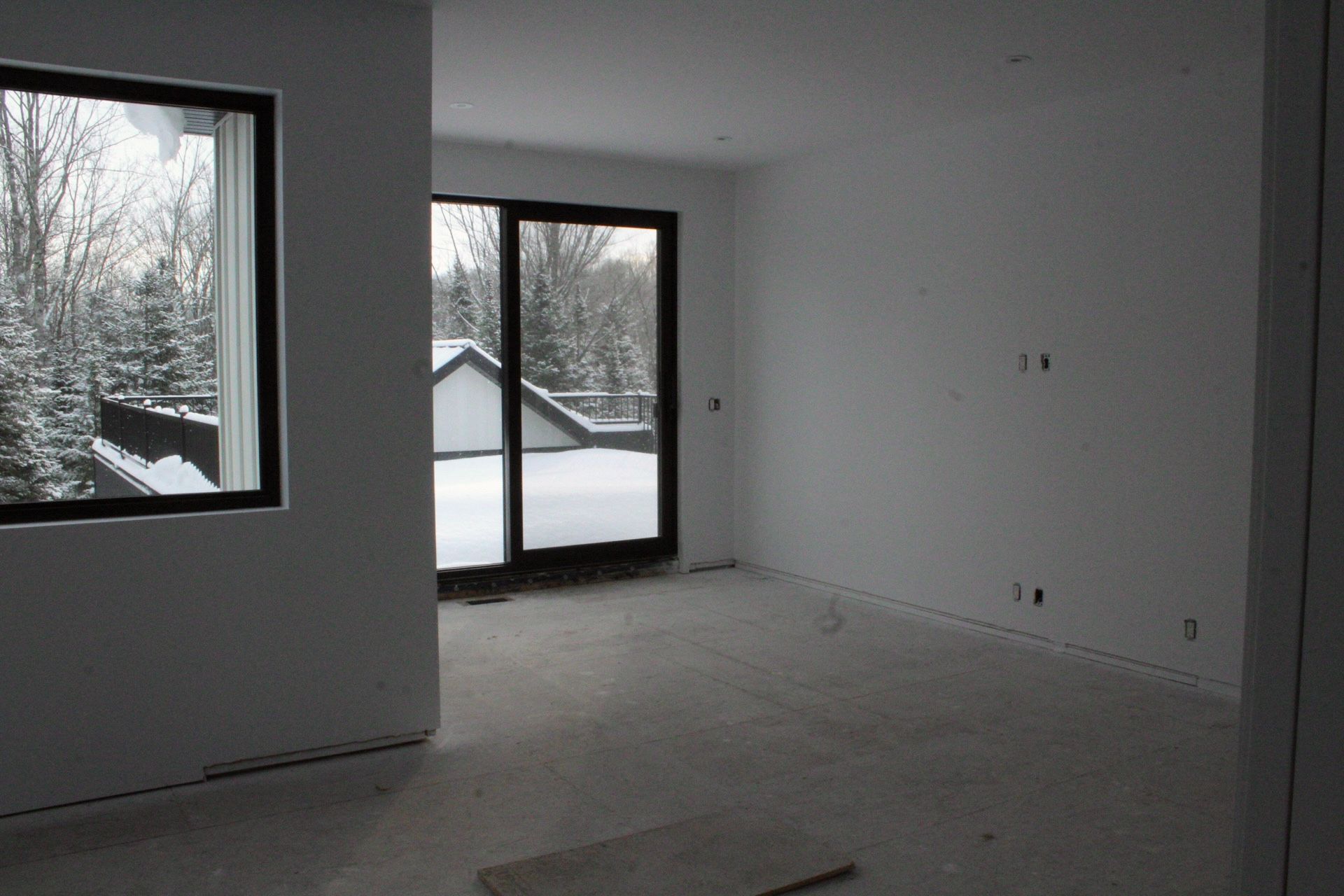 Pièce intérieure vide avec vue enneigée à travers la fenêtre et les portes coulissantes en verre.