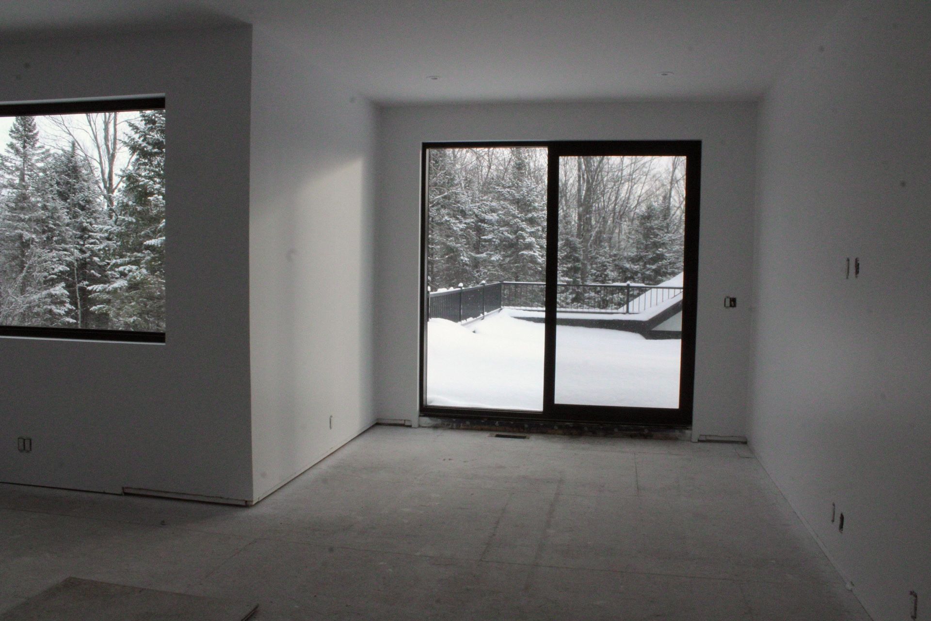 Chambre vide avec grande fenêtre et porte coulissante en verre donnant sur les arbres enneigés.
