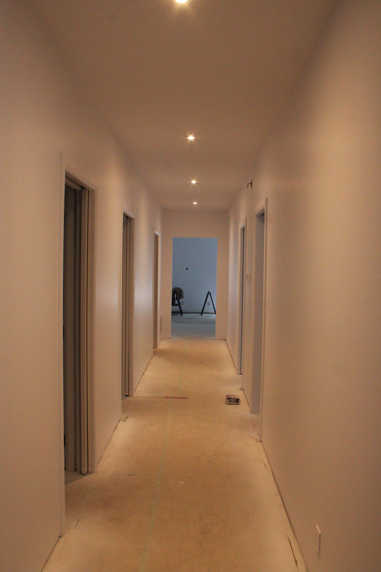 Long couloir blanc avec plusieurs portes et plafonniers encastrés.