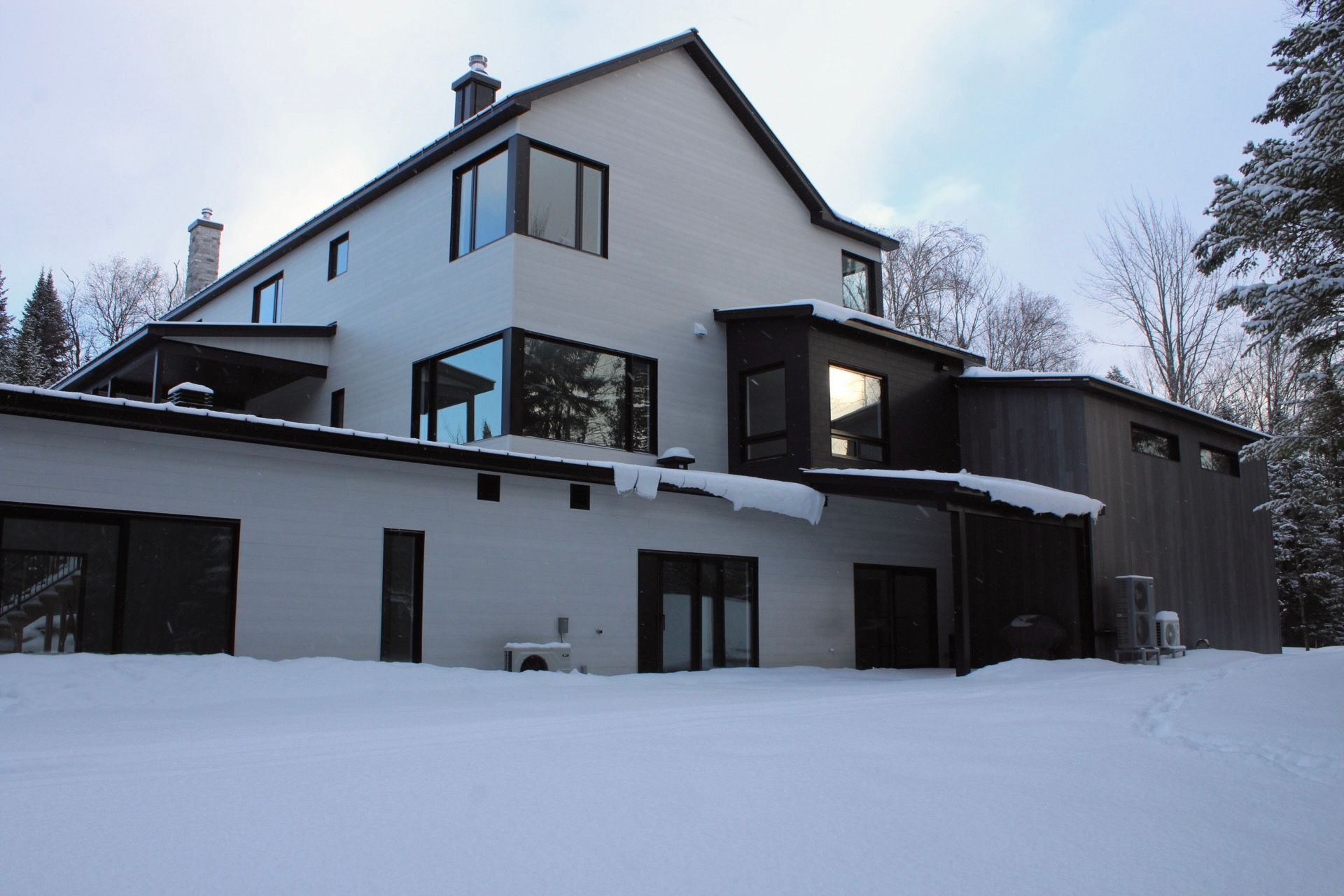 Maison blanche avec des boiseries sombres et de grandes fenêtres dans un décor enneigé.