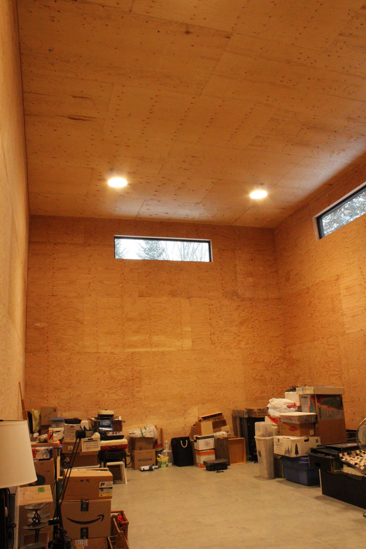 Pièce vide avec des murs et un plafond lambrissés, de petites fenêtres et des boîtes et des objets encombrant le sol.