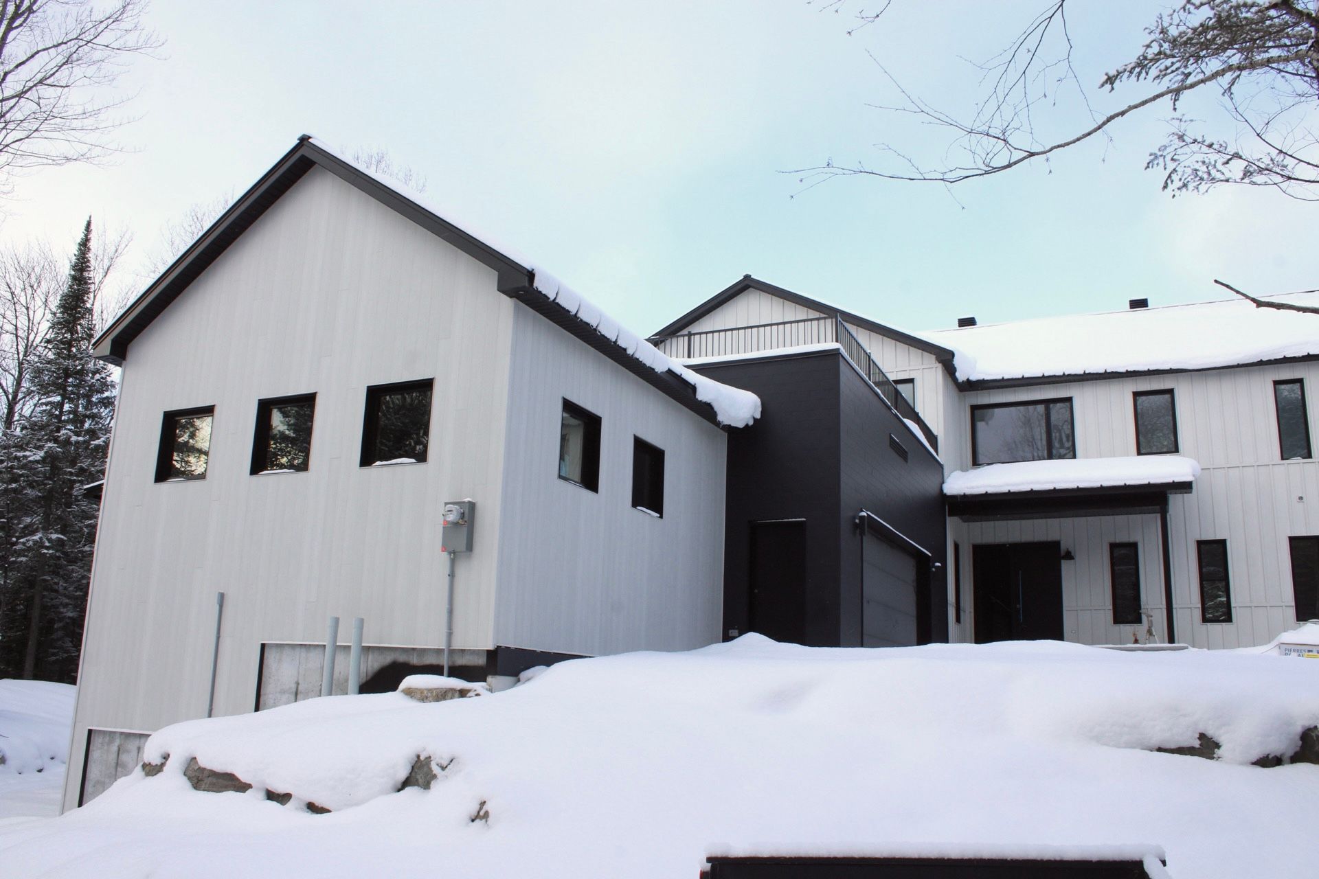 Maison moderne blanche aux accents sombres, recouverte de neige, décor hivernal.