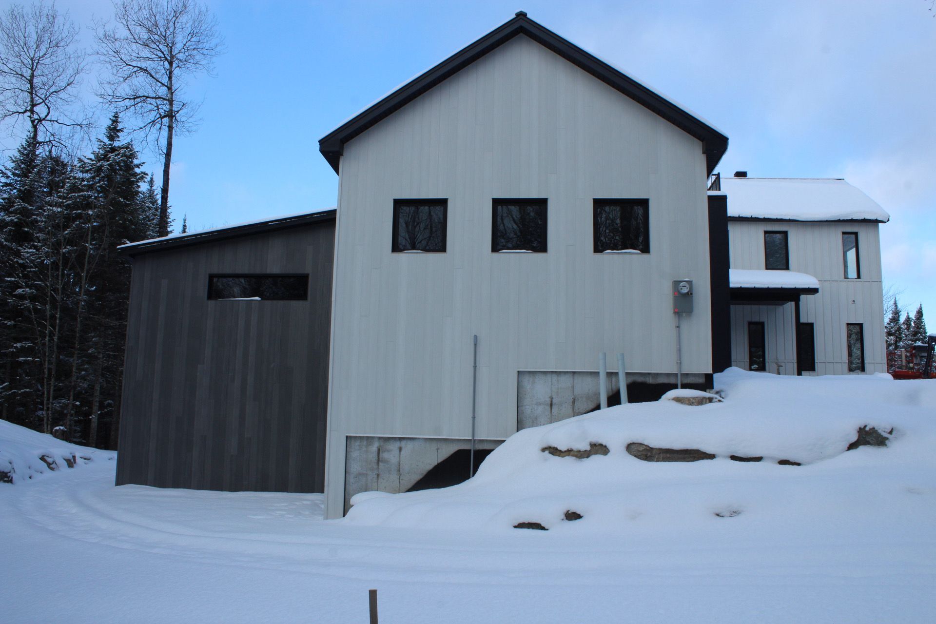 Maison moderne blanche et grise avec des garnitures noires et un environnement enneigé.