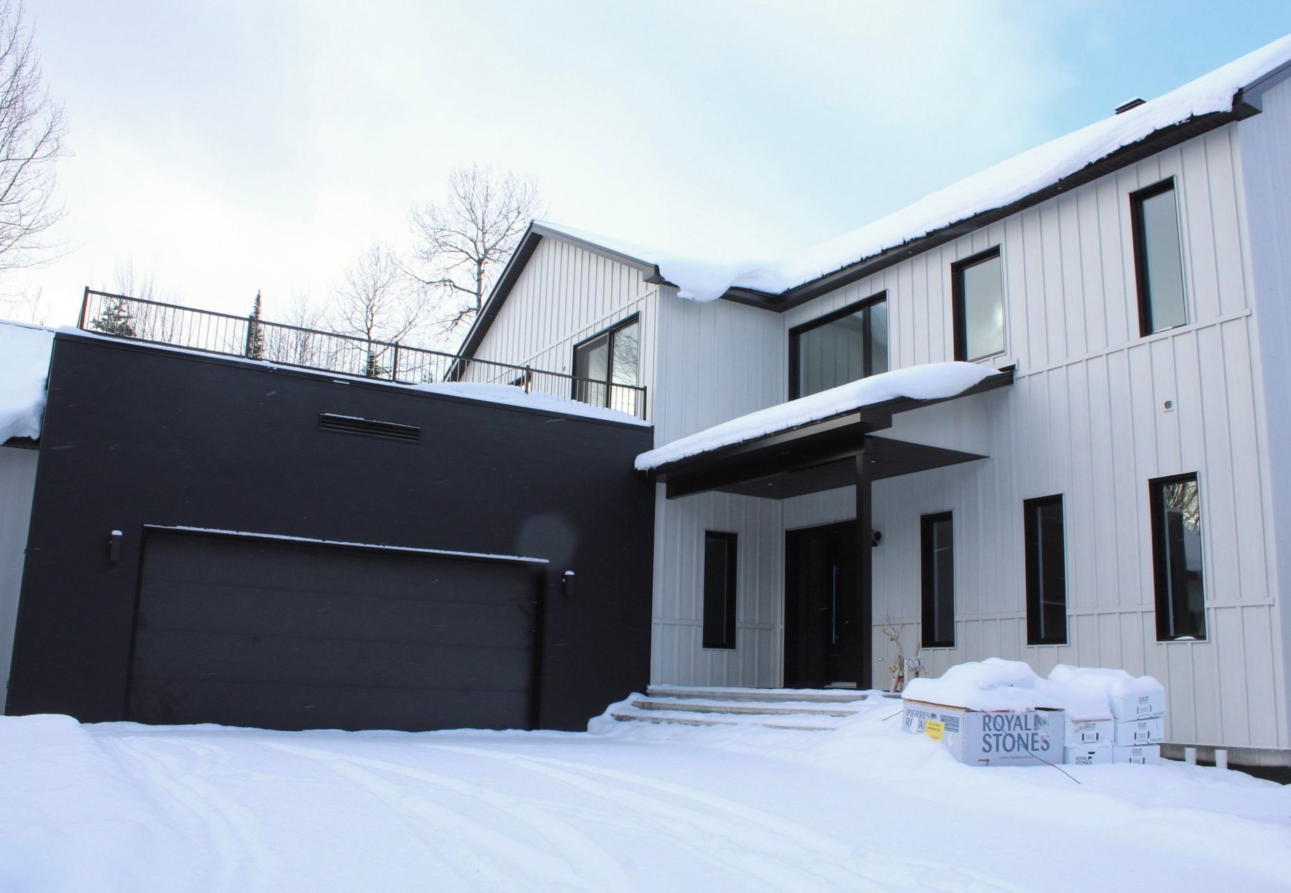 Maison blanche moderne avec une porte de garage noire, recouverte de neige.