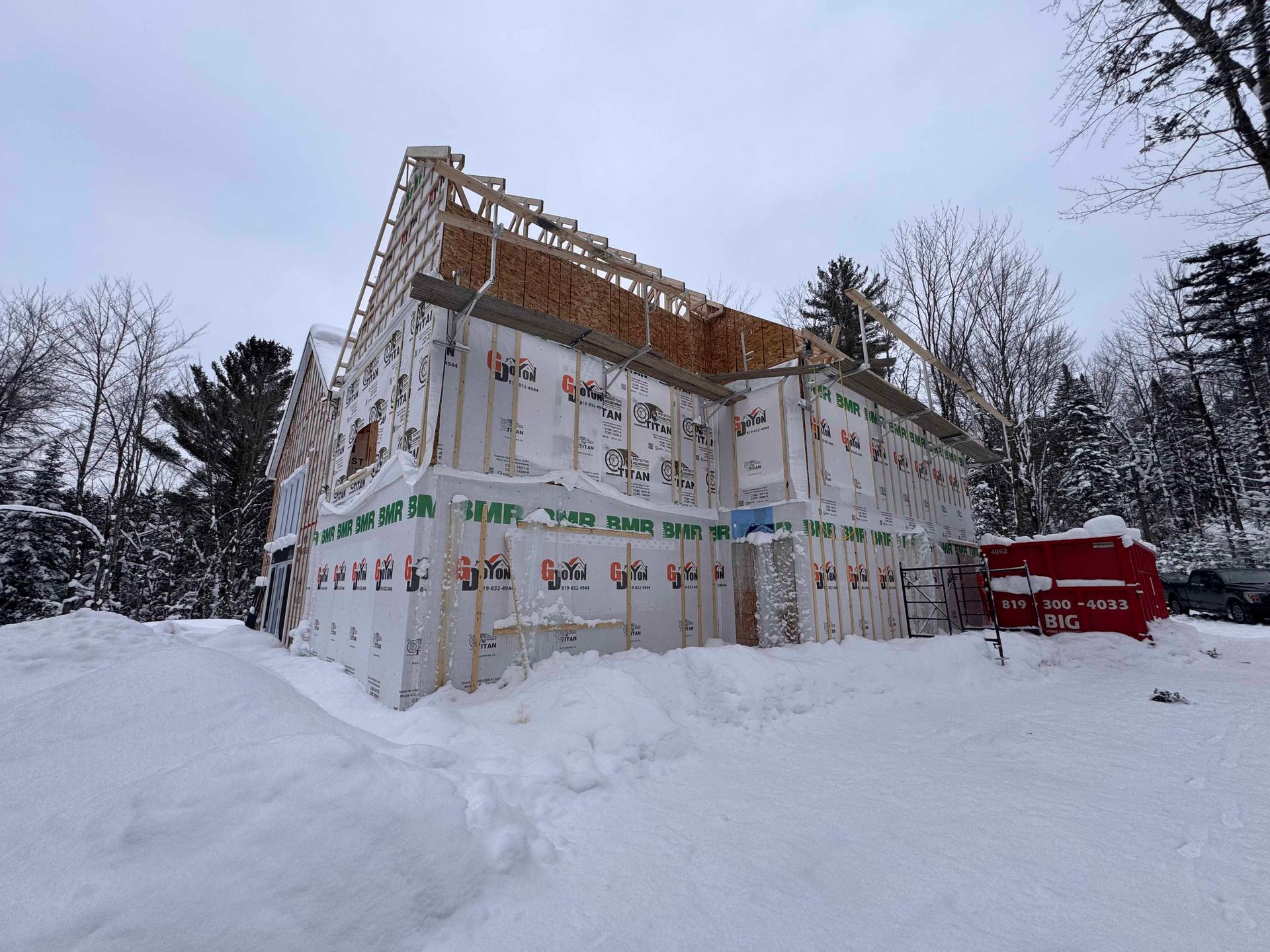 Chantier : maison à ossature bois avec pare-vapeur, fermes de toit et terrain enneigé dans un décor hivernal.